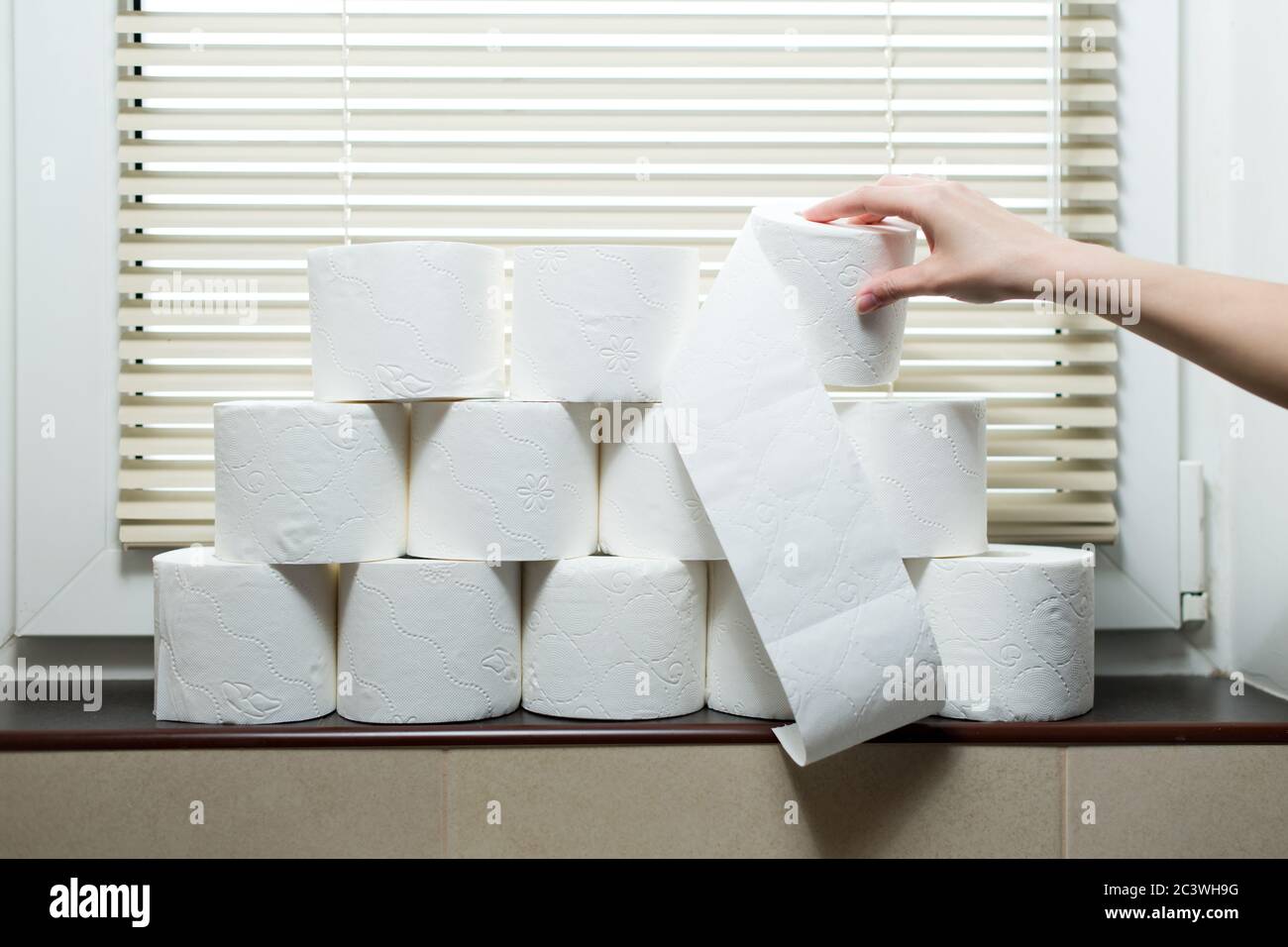 Une main prend un rouleau de papier toilette du seuil de fenêtre dans les toilettes Banque D'Images