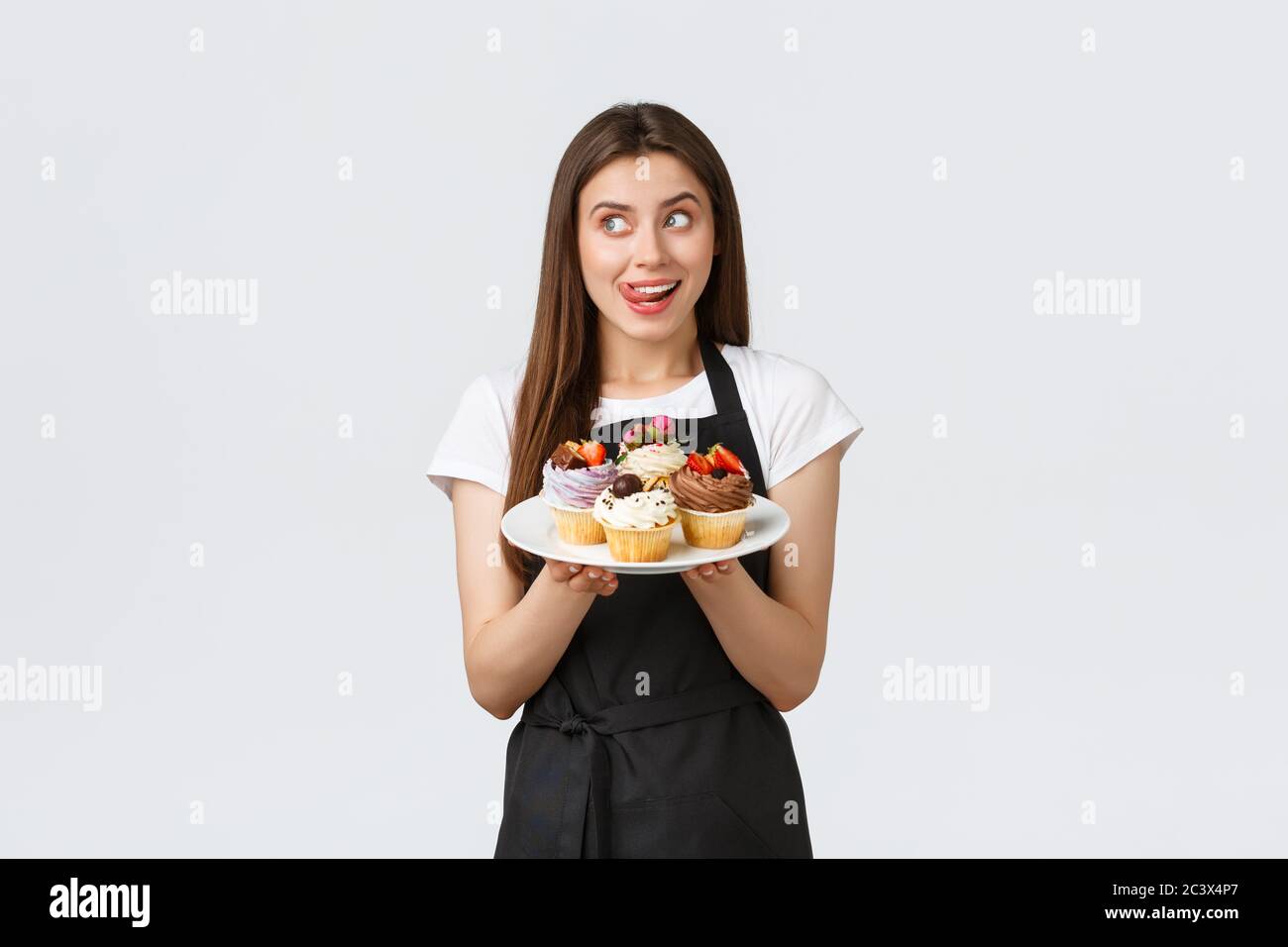 Concept des employés d'épicerie, des petites entreprises et des cafés. Une jolie femme de barista excitée dans une assiette à plateau noire avec de délicieux petits gâteaux et Banque D'Images