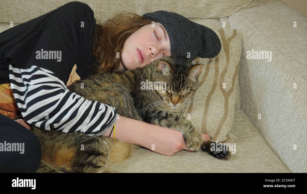 Une adolescente se nappant sur un canapé tout en embrassant son chat Banque D'Images