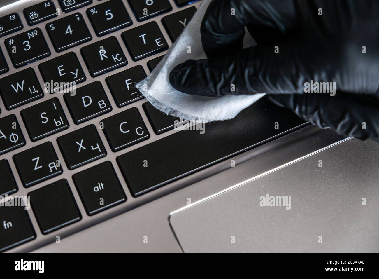 Nettoyage du clavier de l'ordinateur portable avec des lingettes humides antibactériennes. Gant noir et serviette blanche sur un ordinateur noir. Éliminer la poussière et tuer les bactéries Banque D'Images