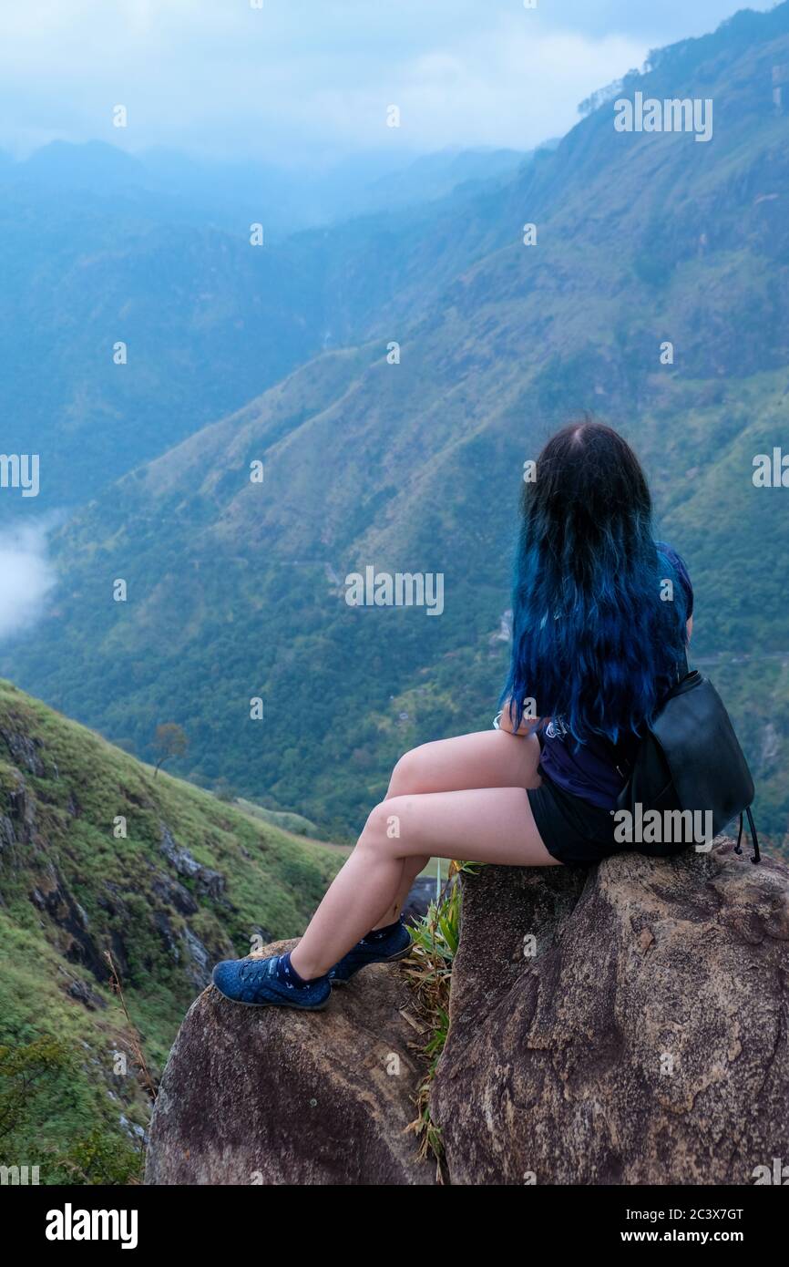 Une jeune fille avec un long cheveux bleu et un sac à dos noir assis sur une falaise. Célèbre montagne dans le sud du Sri Lanka connu sous le nom de Little Adam's Peak. Solitaire Banque D'Images