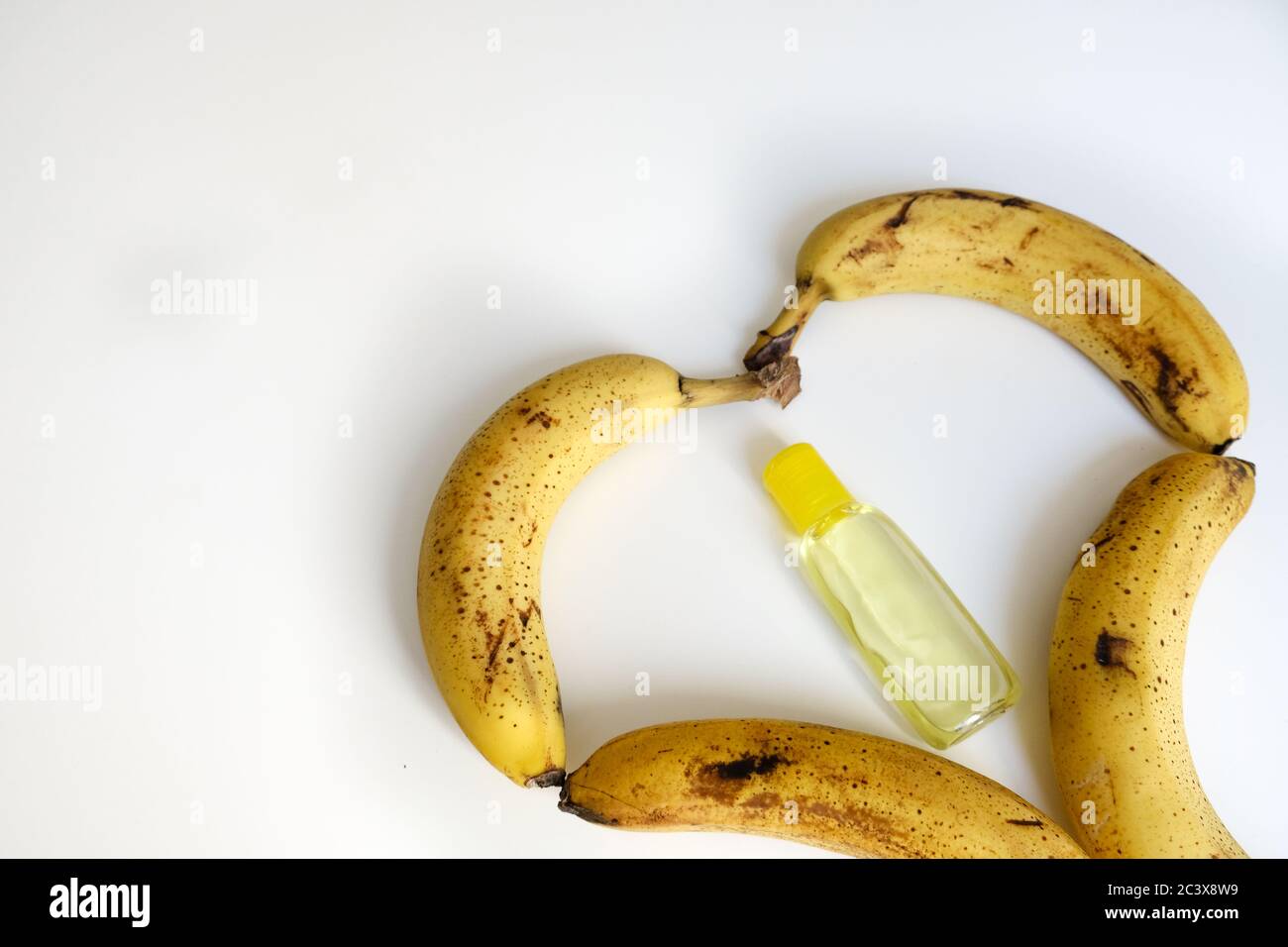Bananes en forme de cœur trop mûres sur une table blanche. Désinfectant pour les mains jaune au milieu. Concept d'auto-soins et de protection du coronavirus. Une alimentation saine Banque D'Images