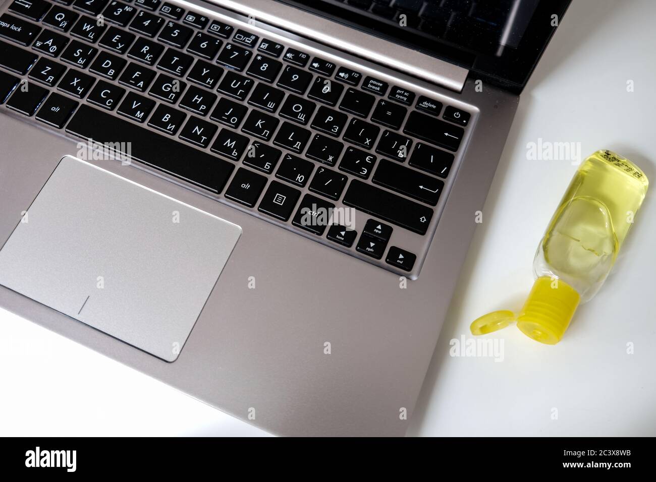 Ouvrez la bouteille jaune d'assainisseur pour les mains près d'un ordinateur portable sur un bureau blanc. Espace de travail de bureau à domicile typique pour prévenir les infections, les bactéries, la grippe et la propagation de virus Banque D'Images