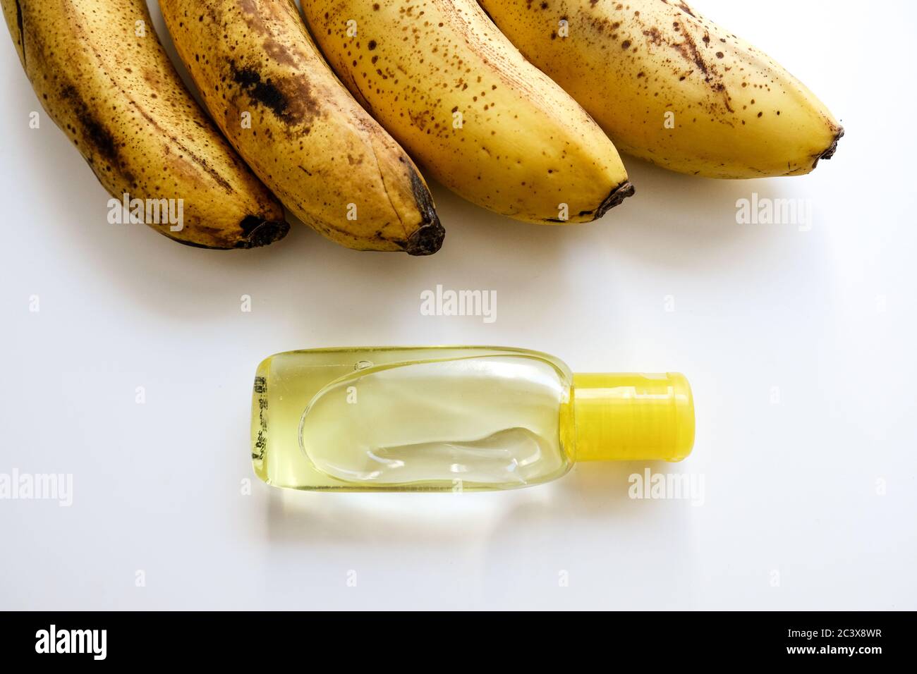 Vue rapprochée d'une rangée de bananes jaunes et d'une bouteille de désinfectant pour les mains sur un bureau blanc. Une alimentation saine pour une bonne immunité et une bonne propagation du virus Covid-19 Banque D'Images