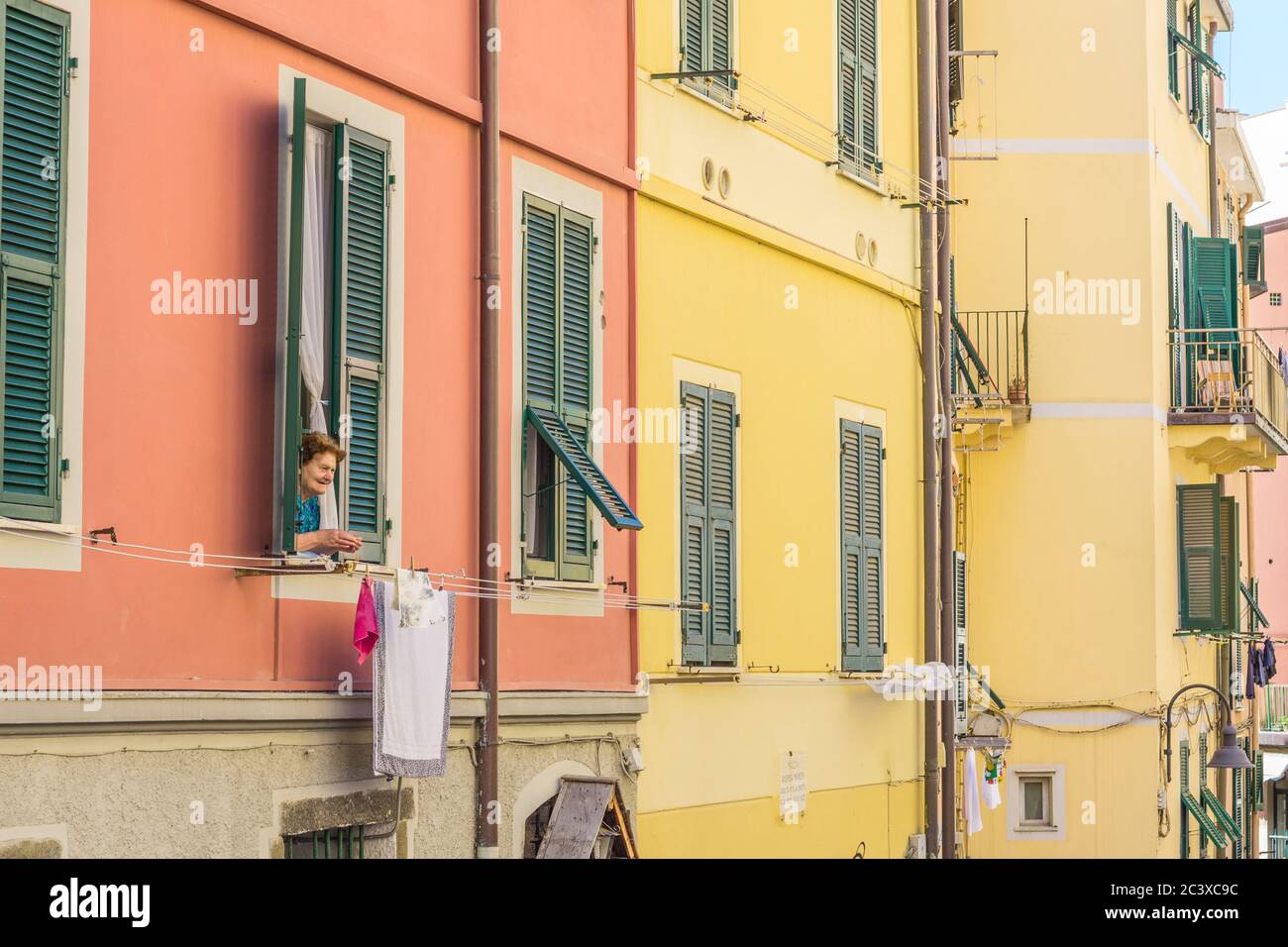 Femme italienne âgée, vue par sa fenêtre sur la rue en dessous. Lavage suspendu à une ligne de lavage. Prise en été Banque D'Images