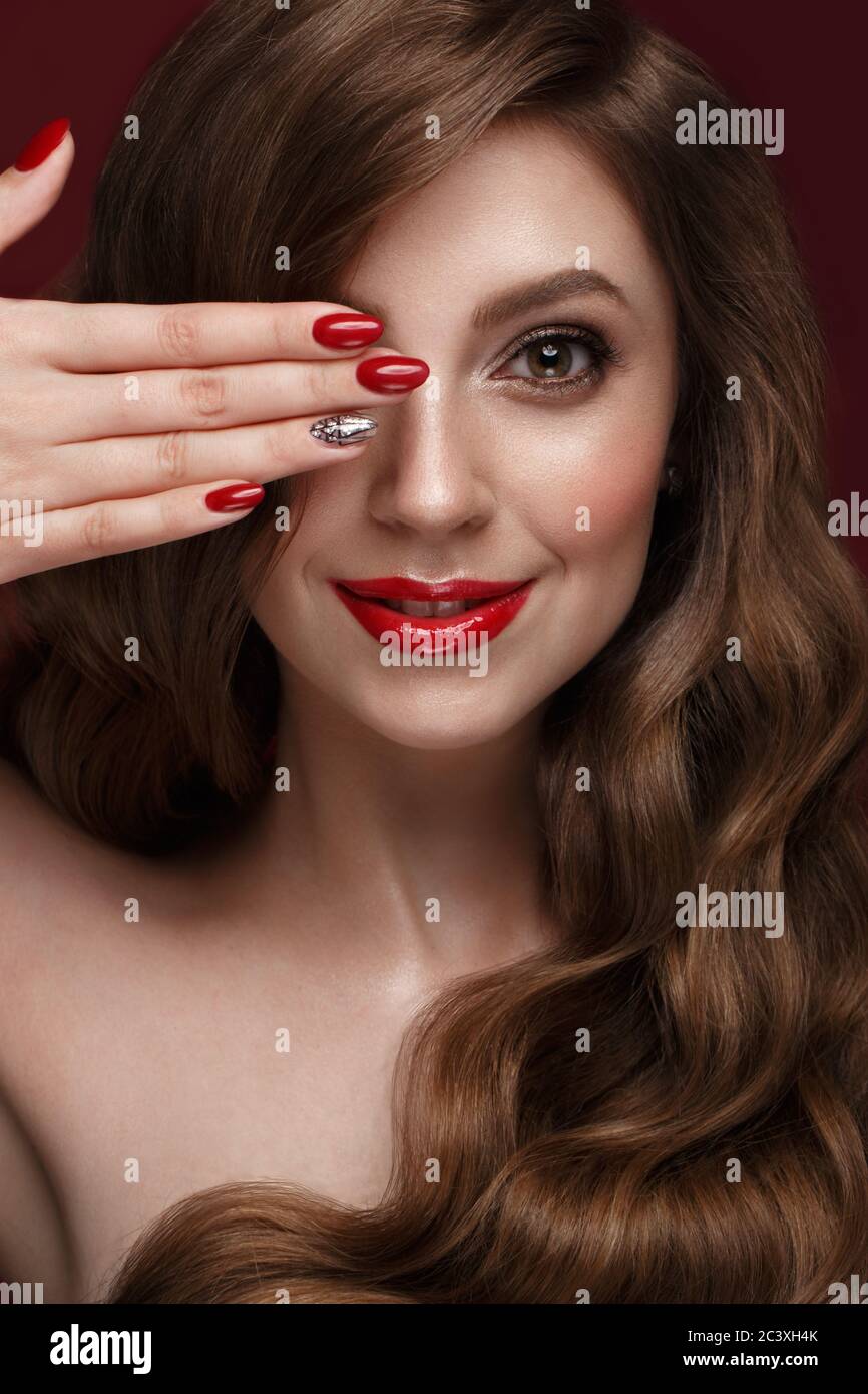Belle fille avec un classique de la forme, des cheveux de boucles et des ongles rouges. Conception manucure. Visage de beauté. Banque D'Images
