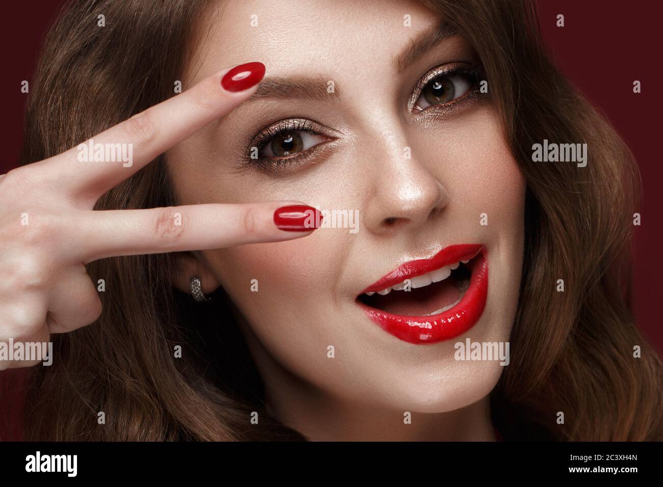 Belle fille avec un classique de la forme, des cheveux de boucles et des ongles rouges. Conception manucure. Visage de beauté. Banque D'Images