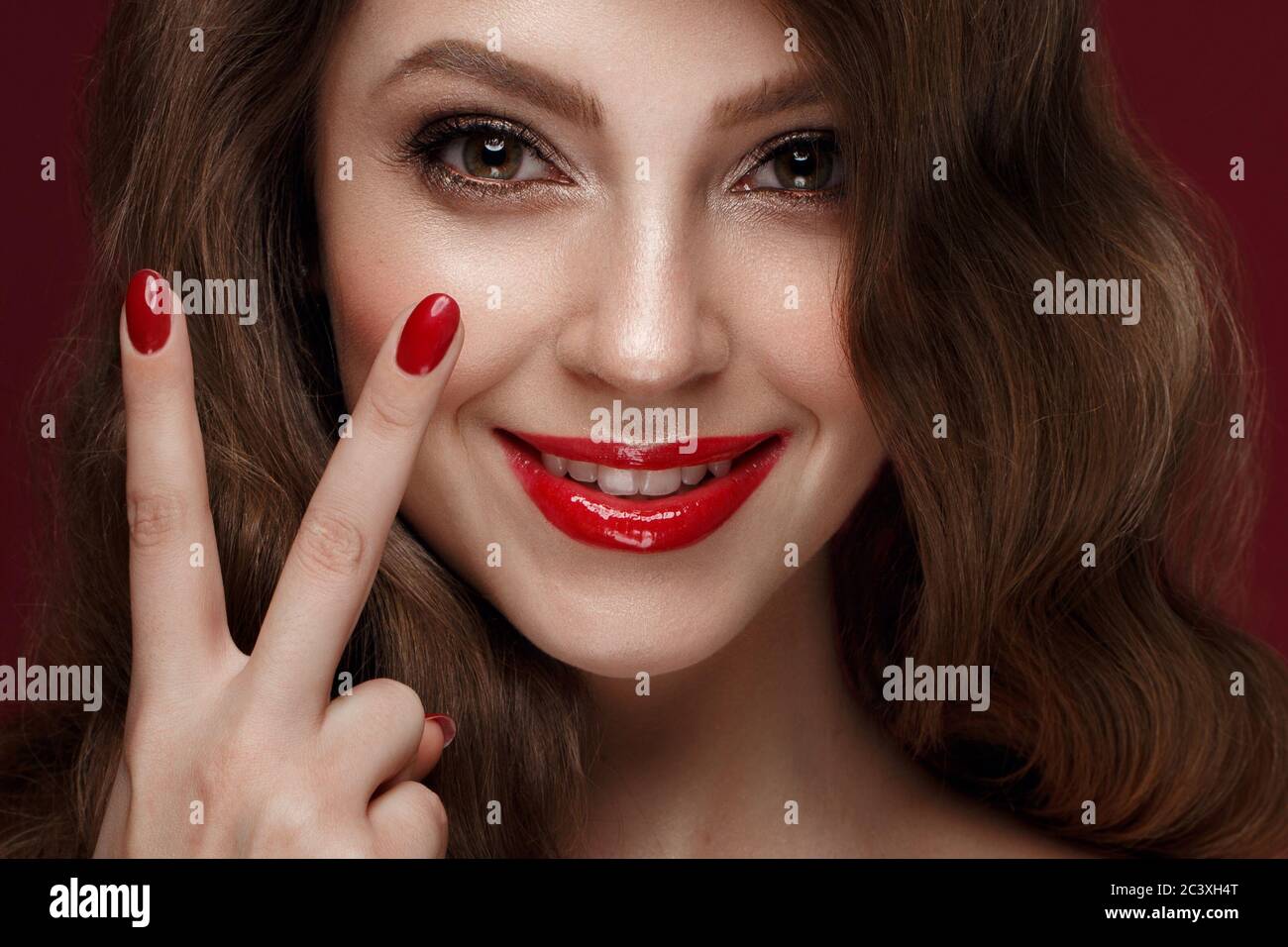 Belle fille avec un classique de la forme, des cheveux de boucles et des ongles rouges. Conception manucure. Visage de beauté. Banque D'Images