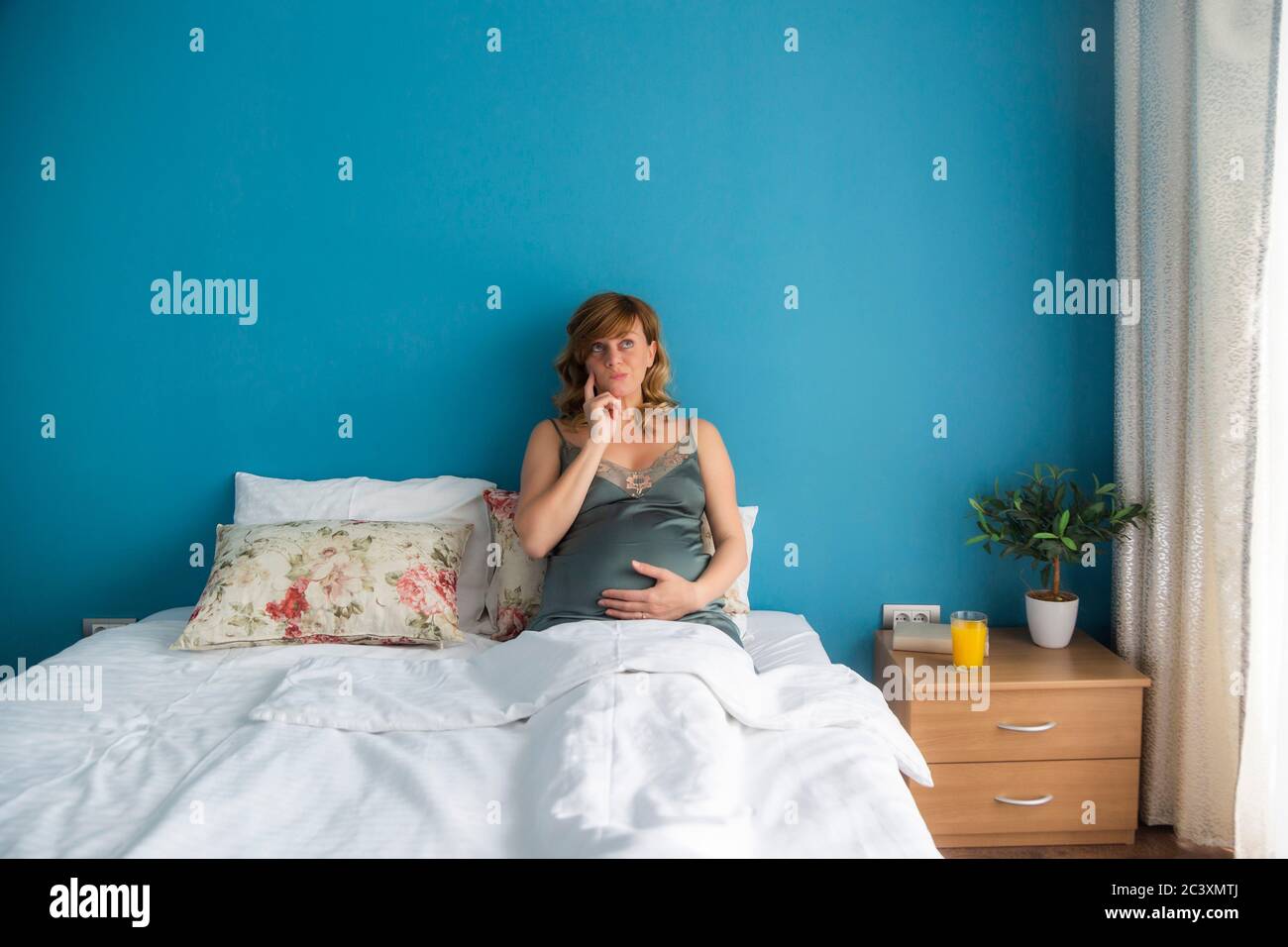 Une femme enceinte en position semiassise au lit avec ses mains autour