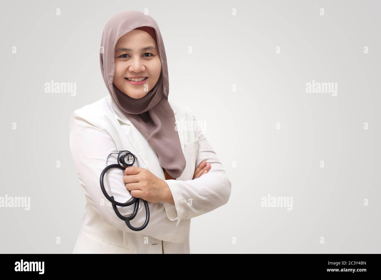 Femme musulmane médecin portant le hijab et le costume, debout avec bras croisés et tenant le stéthoscope, personne réussie et confiante, sur fond blanc Banque D'Images