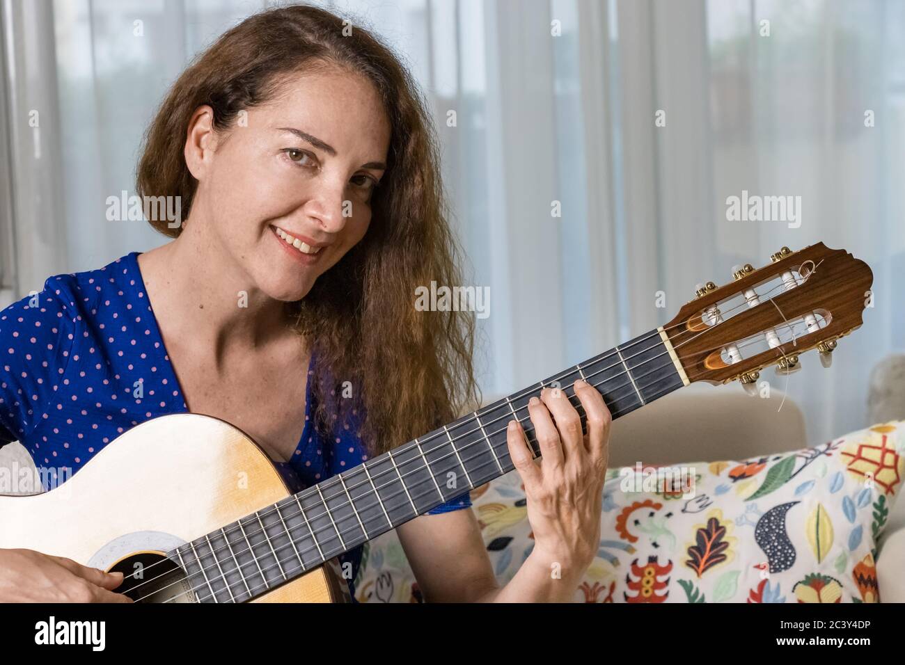 Gros plan d'une enseignante de guitare jouant une guitare acoustique à la maison, regardant un appareil photo Banque D'Images