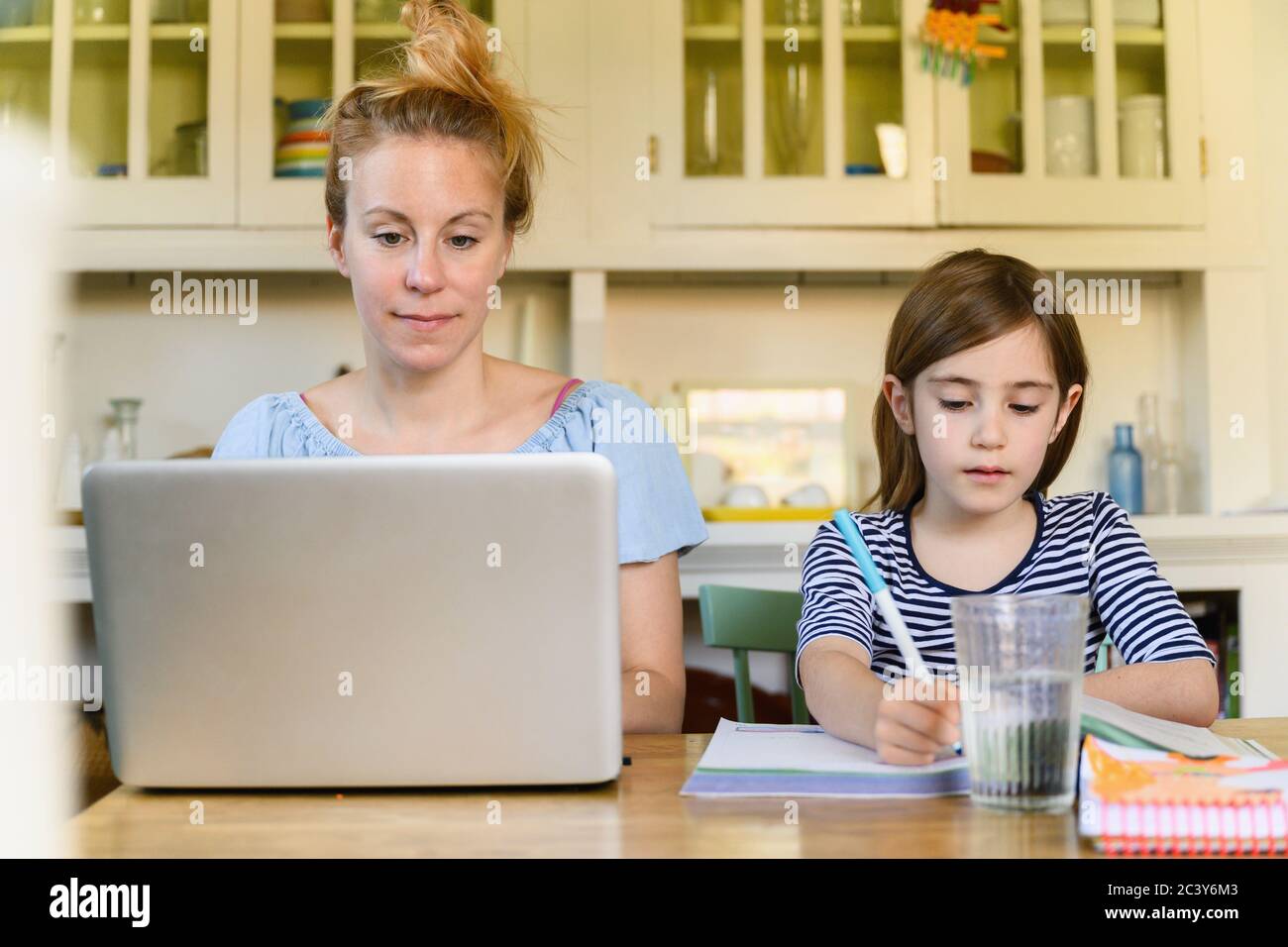 Femme travaillant sur ordinateur portable et fille (6-7) faisant des devoirs Banque D'Images