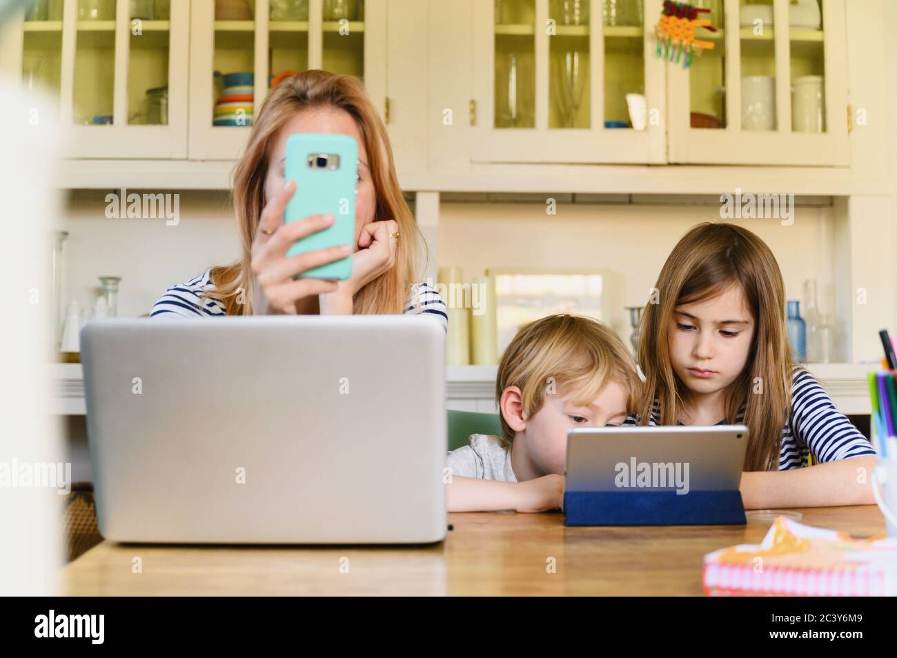 Femme tenant un smartphone devant un ordinateur portable pendant qu'elle était garçon (4-5) et fille (6-7) utilisant une tablette numérique Banque D'Images