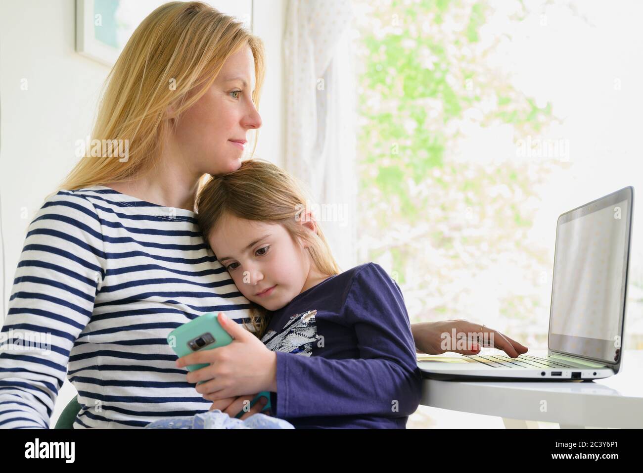 La mère travaille sur un ordinateur portable alors que la fille (6-7) utilise un smartphone Banque D'Images