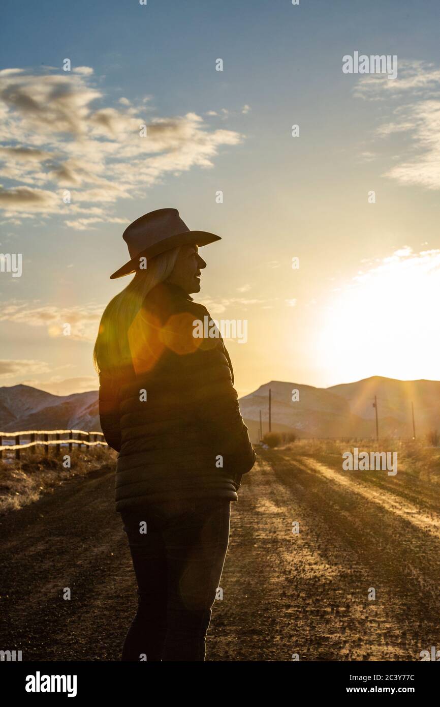 USA, Idaho, Sun Valley, femme en chapeau de cowboy debout sur la route de terre au coucher du soleil Banque D'Images