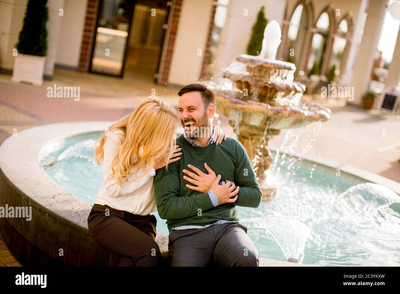Portrait d'un beau couple d'amour souriant assis près d'une fontaine par un beau jour Banque D'Images