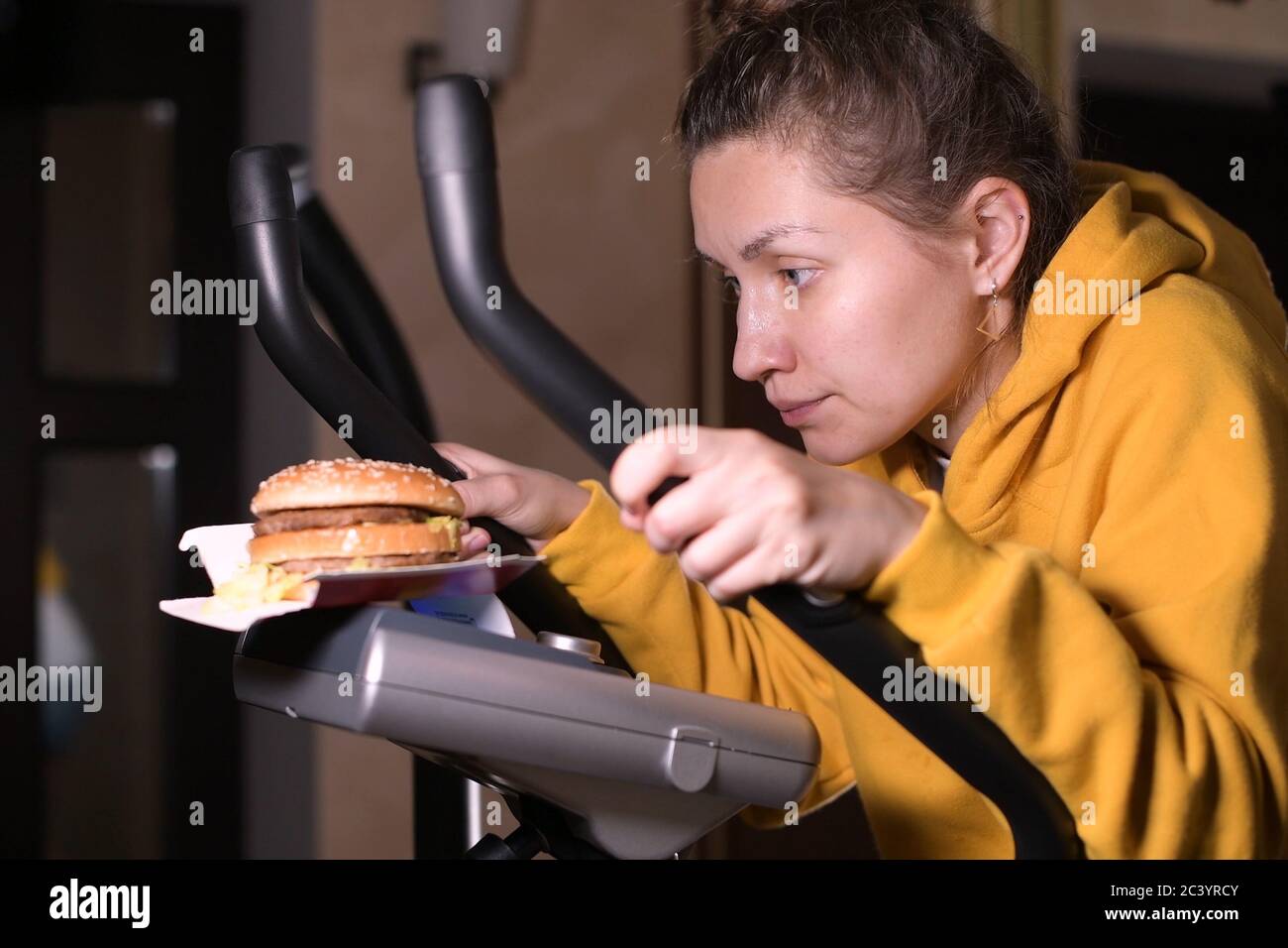 Une fille s'entraîne dans la sueur et regarde le hamburger, qui se trouve en face d'elle Banque D'Images
