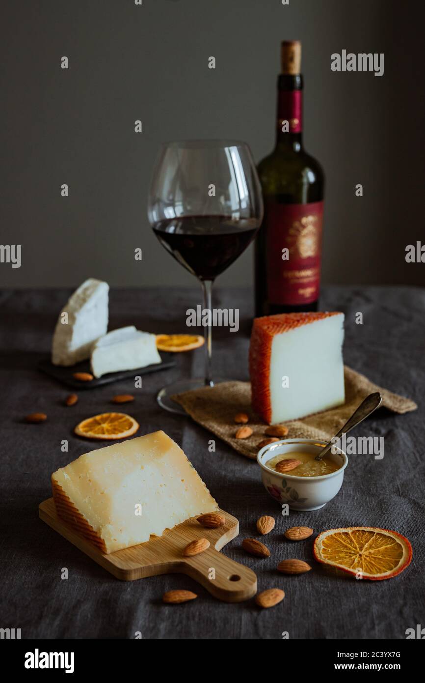 Une photo verticale d'une vie encore en chèvre, brebis et brie, amande, miel, tranches d'orange, une bouteille et un verre de vin rouge Banque D'Images