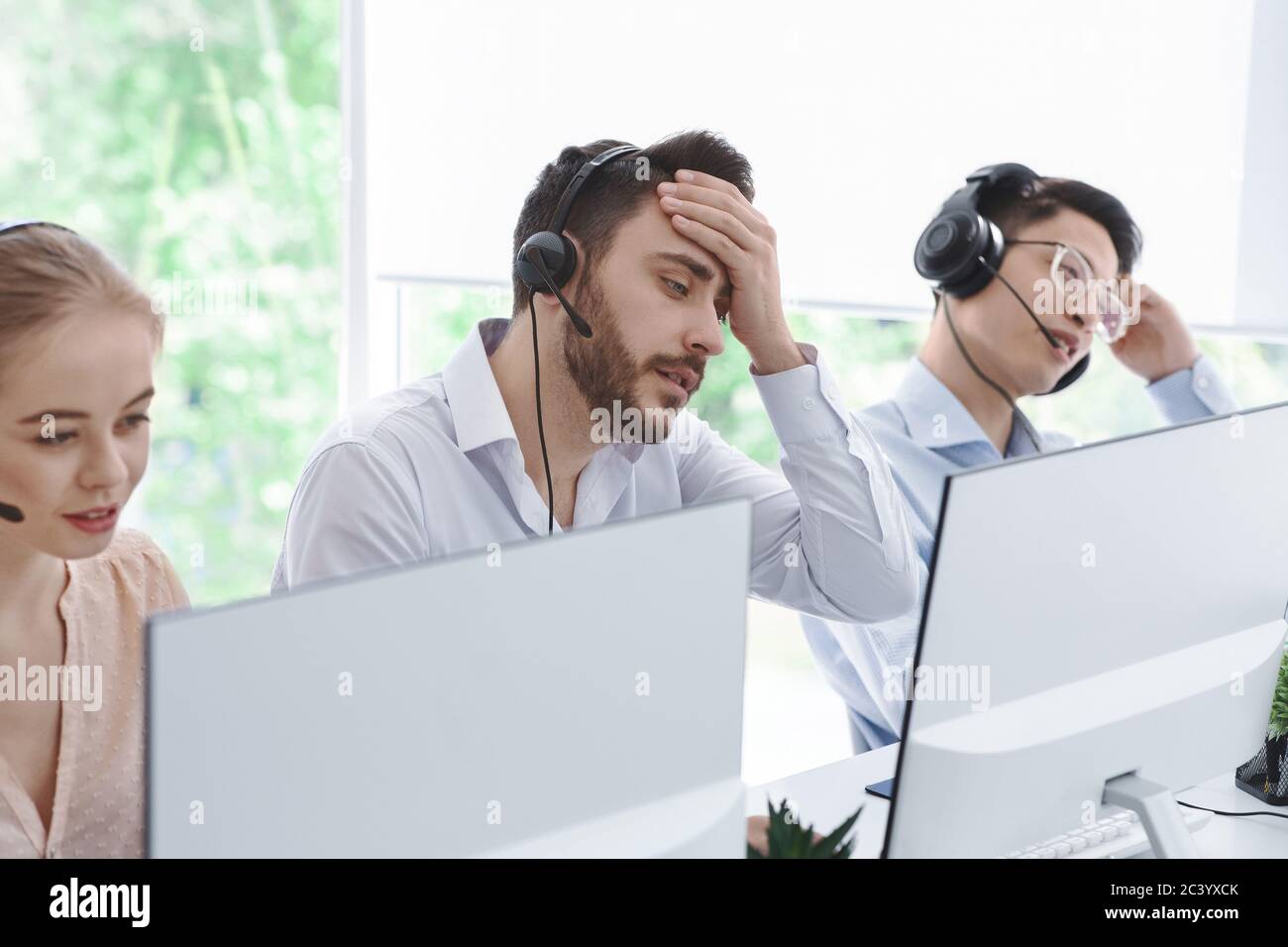 Un opérateur de centre d'appels fatigué et ses collègues communiquent avec les clients dans un bureau à espace ouvert Banque D'Images