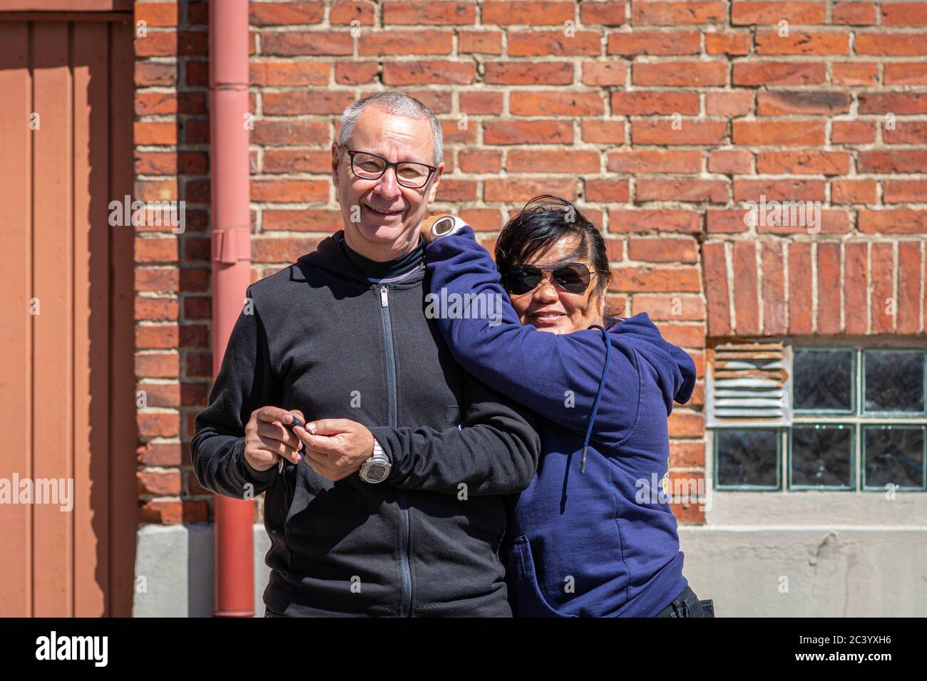 Un couple d'âge moyen (50+) mixte racial (caucasien et asiatique) se fait une excursion ensemble. Mur en brique rouge en arrière-plan Banque D'Images