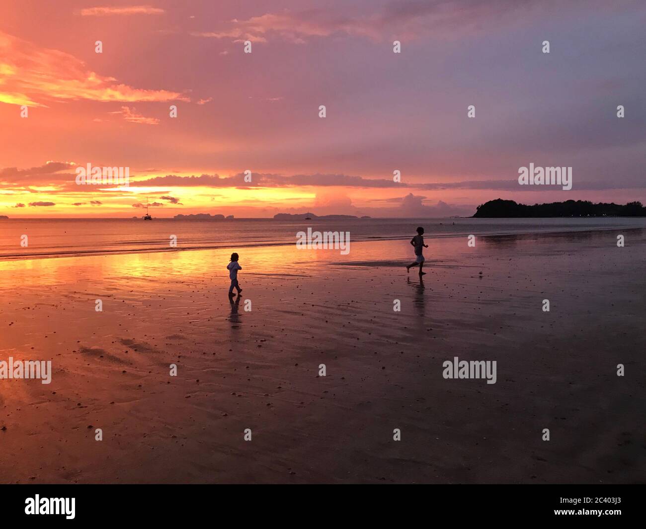 les enfants courent sur le sable au bord de l'océan au coucher du soleil. Banque D'Images