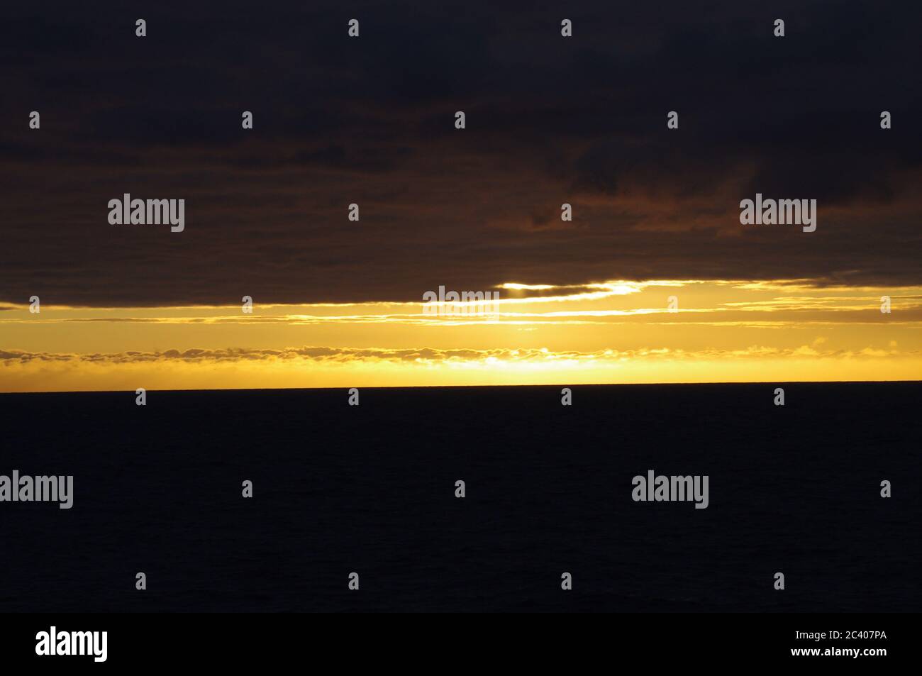 Coucher de soleil sur nuages sombres et mer, rayure horizon brillante entre les nuages sombres et la mer, séquence d'images de coucher de soleil émergeant du ciel sombre Banque D'Images