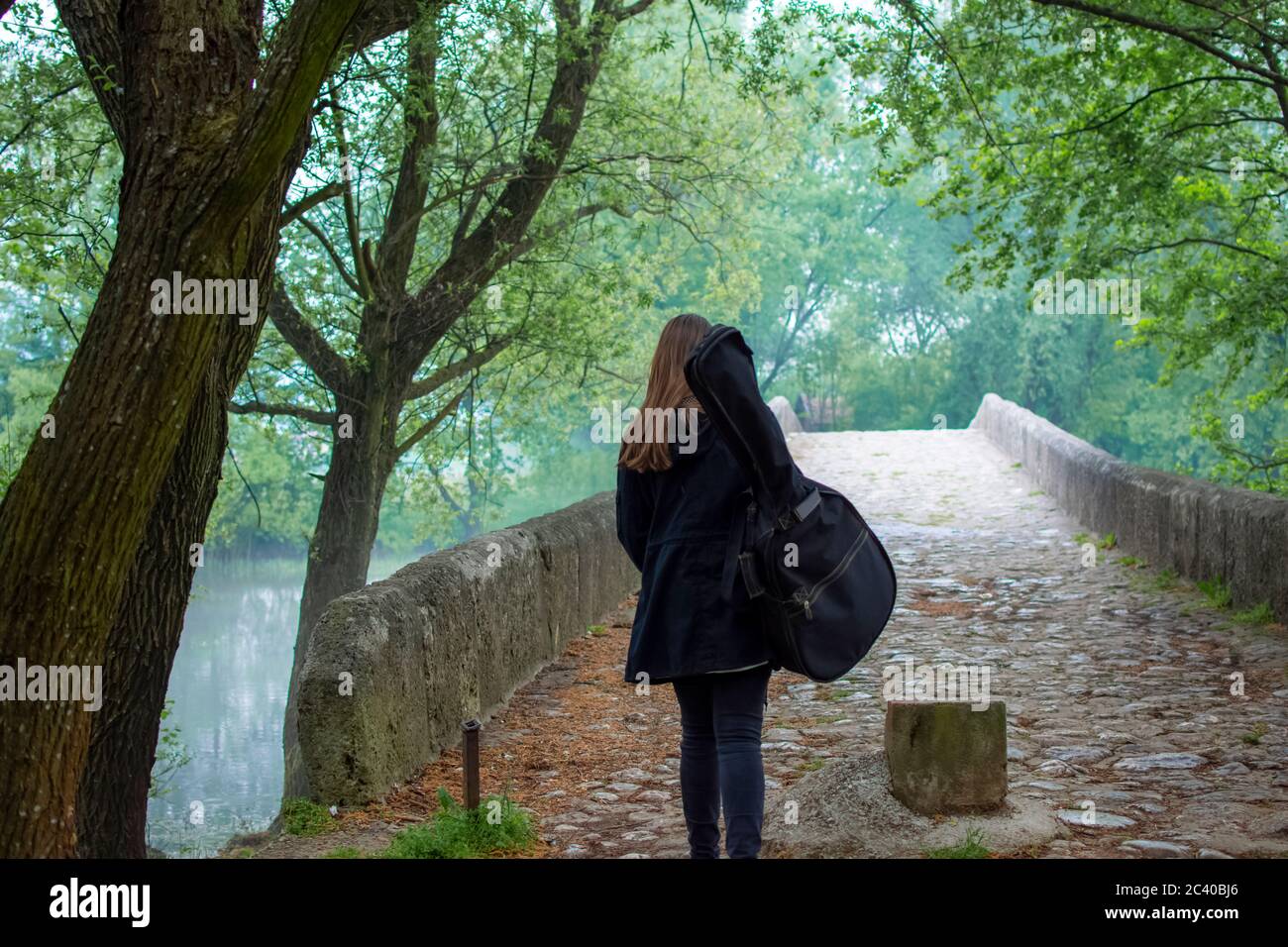 Une jeune fille porte un sac de guitare tout en marchant seule dans la nature Banque D'Images
