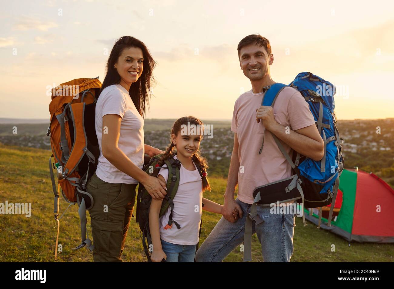 Jeune famille de trois avec sacs à dos au camping en montagne. Parents et fille heureux en vacances d'été Banque D'Images