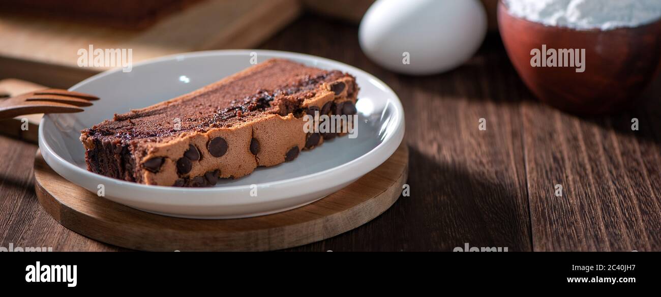 Gâteau éponge traditionnel taïwanais au goût de chocolat (taïwanais castella kasutera) sur une table de fond en plateau de bois avec les ingrédients, gros plan. Banque D'Images