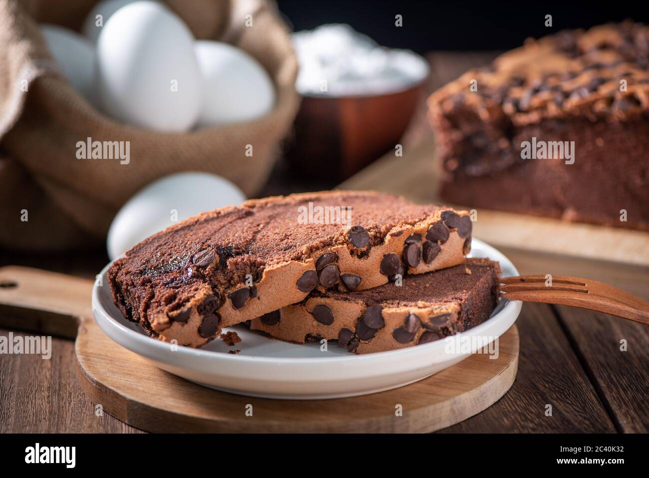 Gâteau éponge traditionnel taïwanais au goût de chocolat (taïwanais castella kasutera) sur une table de fond en plateau de bois avec les ingrédients, gros plan. Banque D'Images