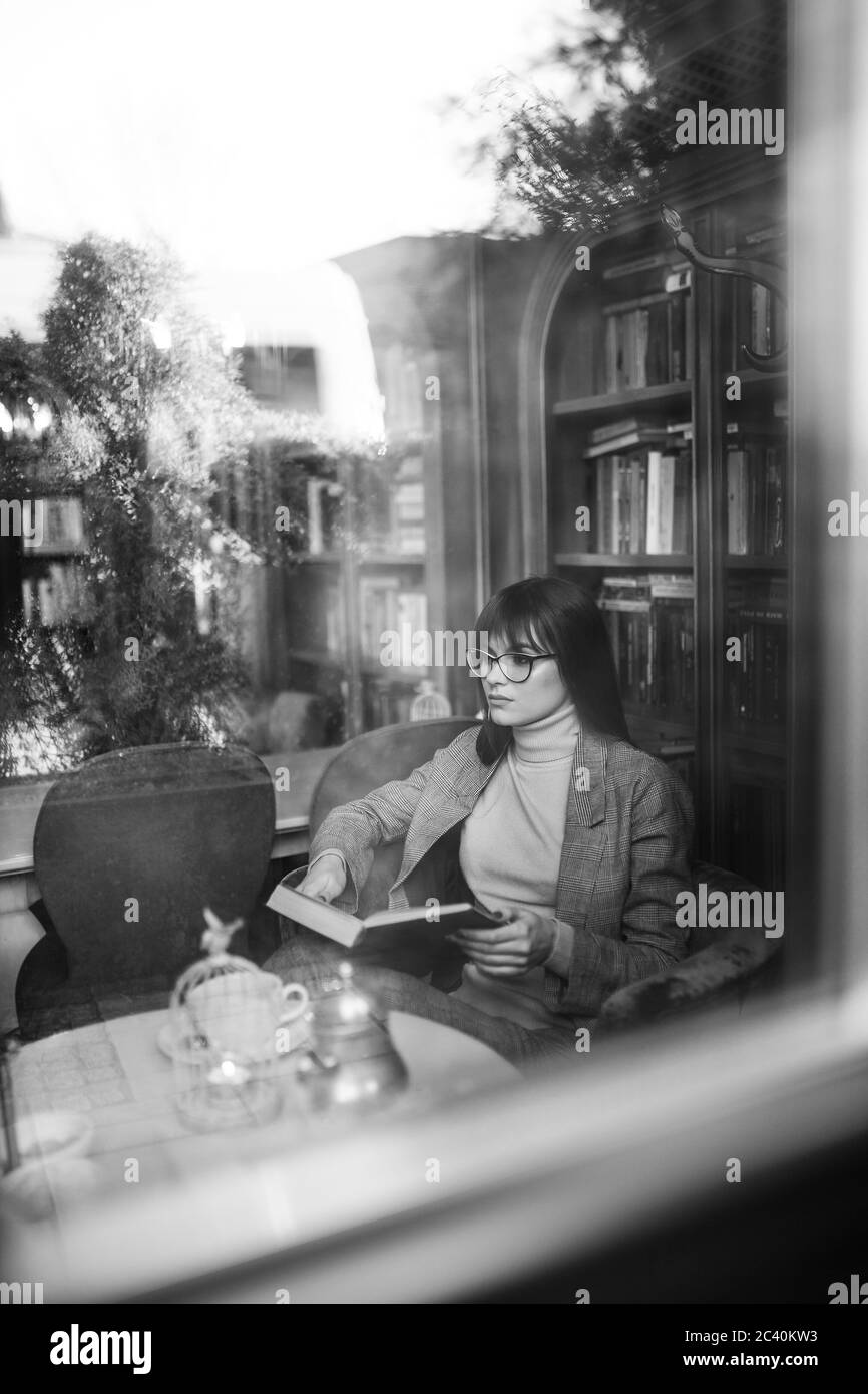 Belle fille rêveuse dans des verres élégants et tranchants. Dans la bibliothèque. Banque D'Images