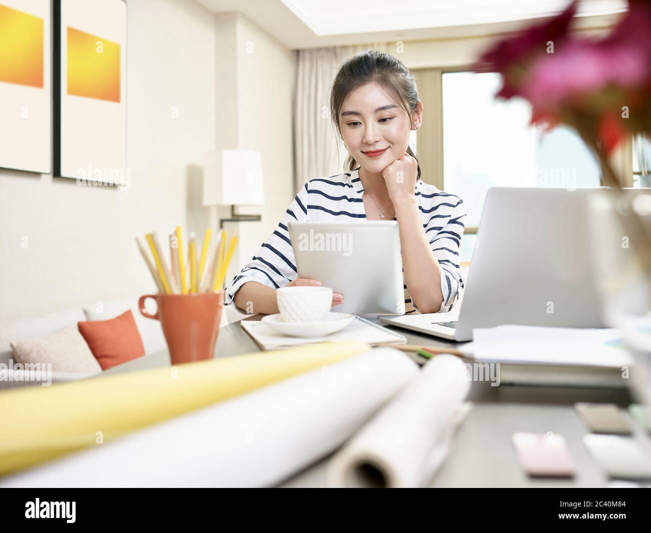 jeune femme d'affaires asiatique travaillant à la maison avec un ordinateur portable et une tablette numérique (œuvres d'art en arrière-plan modifiées numériquement) Banque D'Images