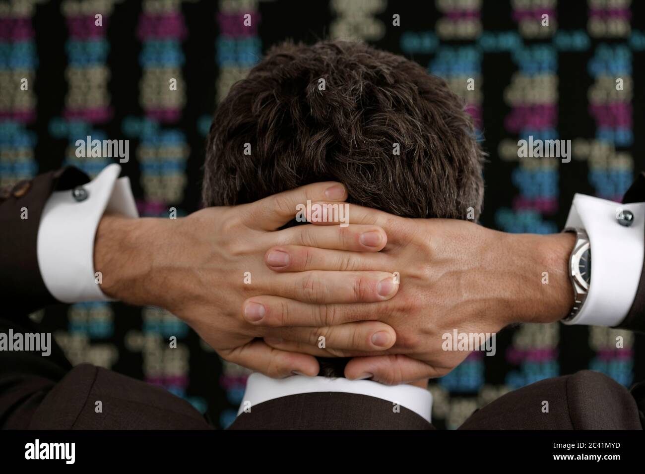 Le courtier en Bourse se tient devant le tableau de bord avec ses mains clapées derrière sa tête Banque D'Images