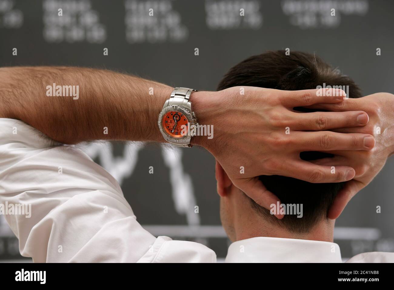 Le courtier en Bourse se tient devant le tableau de bord avec ses mains clapées derrière sa tête Banque D'Images