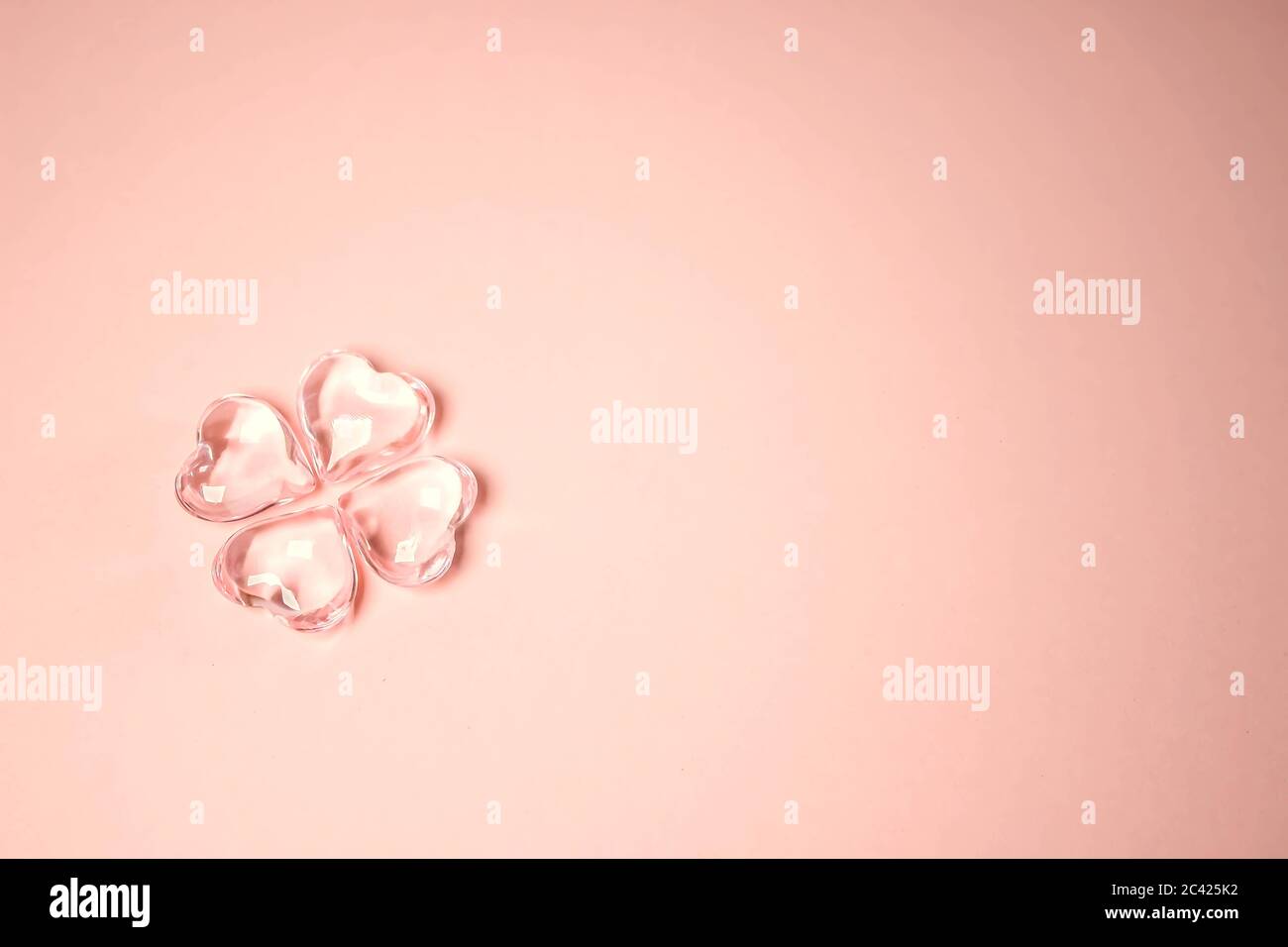 Imitation d'un trèfle à quatre feuilles avec quatre coeurs en verre sur fond rose pour la Saint Patrick. Espace pour le texte, concept de texture numérique Banque D'Images