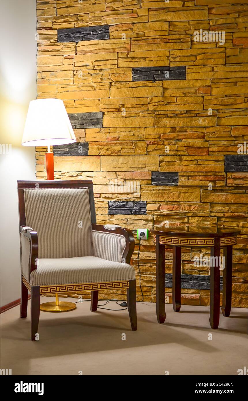 Partie de l'intérieur - coin pour le repos; fauteuil, table d'appoint, lampe et mur en pierre Banque D'Images