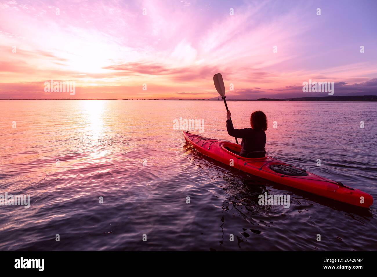 Kayak de mer dans des eaux calmes pendant un coucher de soleil coloré et vibrant. Banque D'Images Kayak de mer dans des eaux calmes pendant un coucher de soleil coloré et vibrant. Banque D'Images