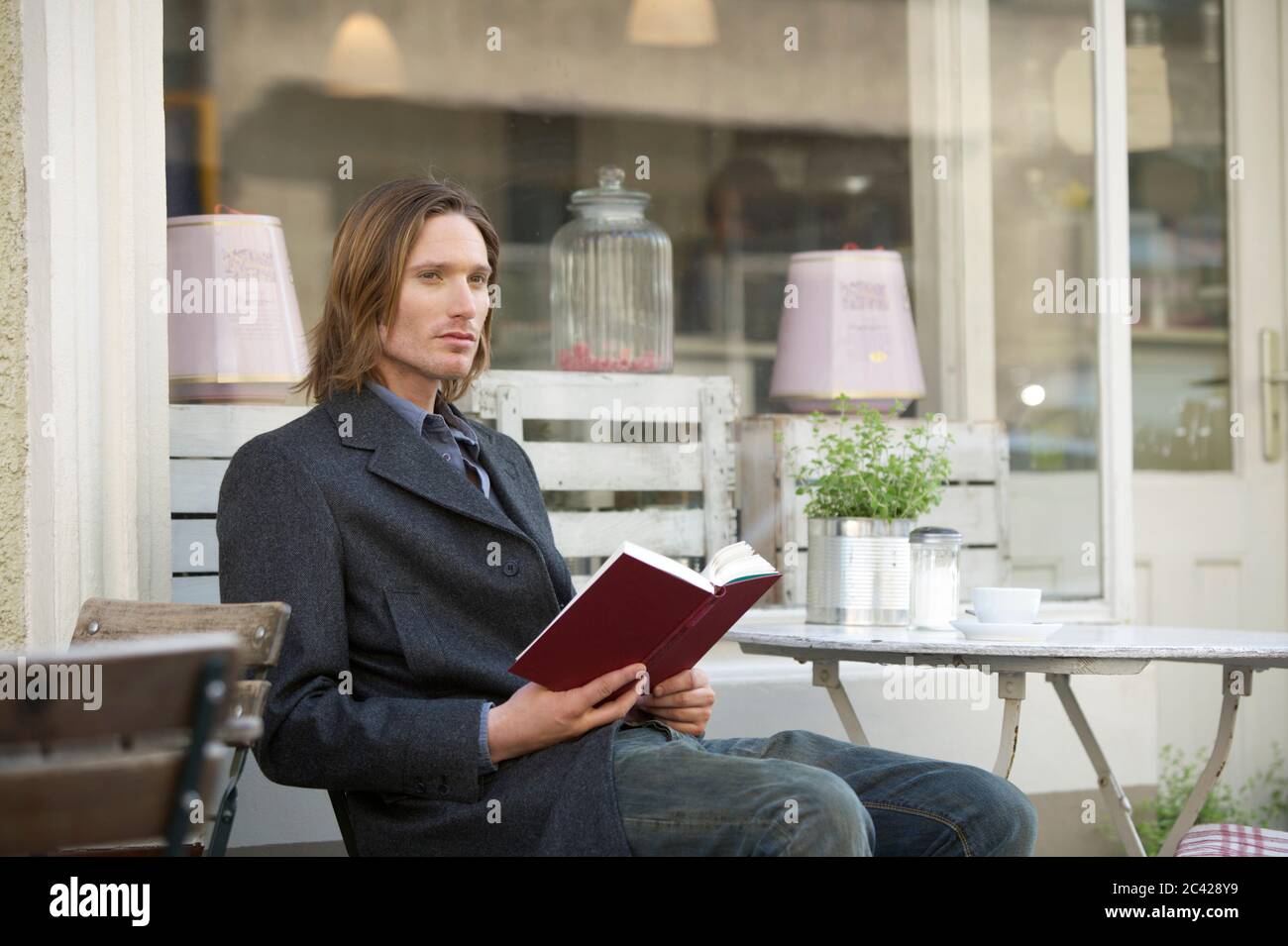 Un jeune homme avec livre est assis dans un café de rue - simple - gastronomie Banque D'Images