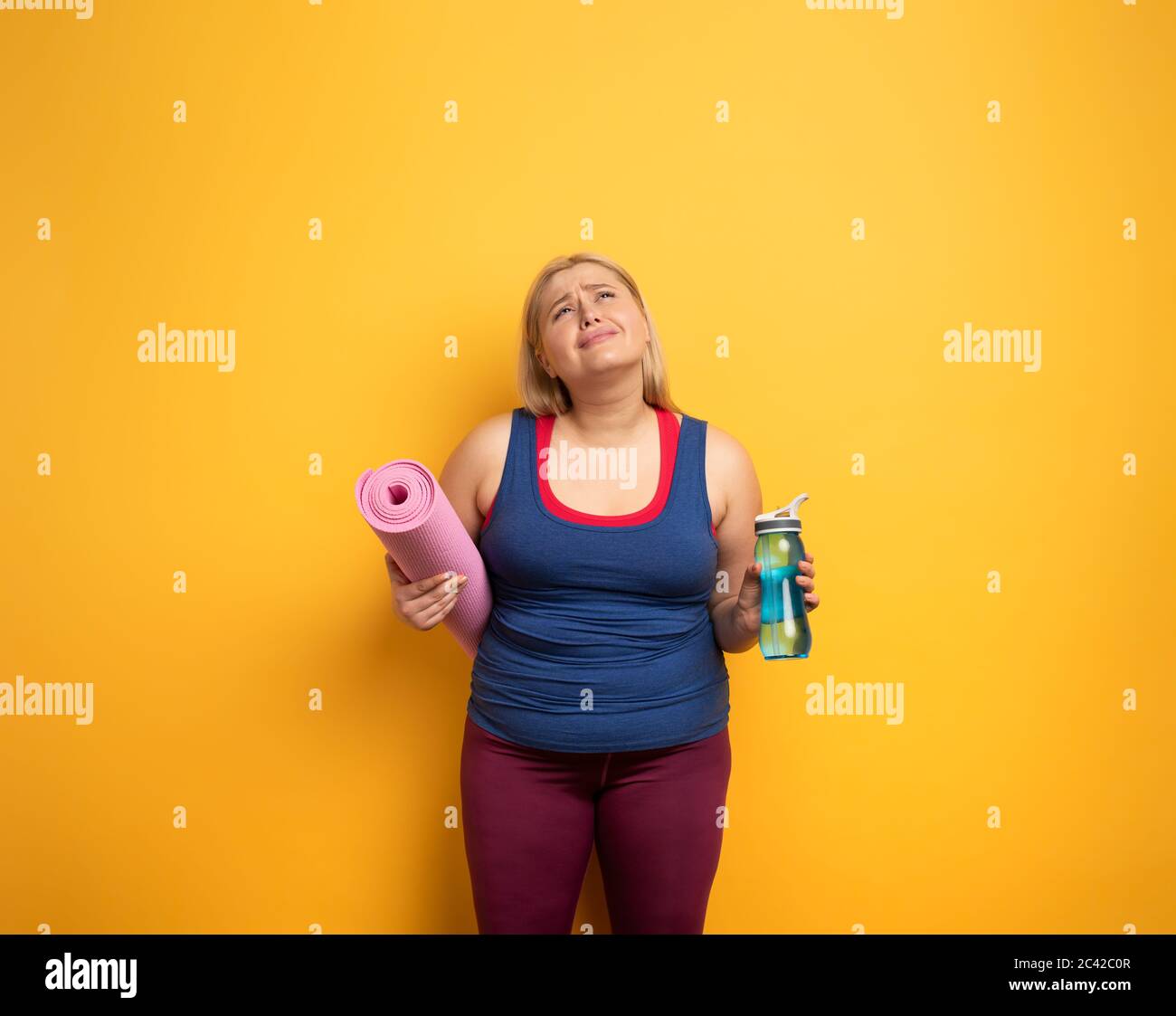 FAT Girl fait de la gym à la maison. Expression fatiguée. Fond jaune Banque D'Images