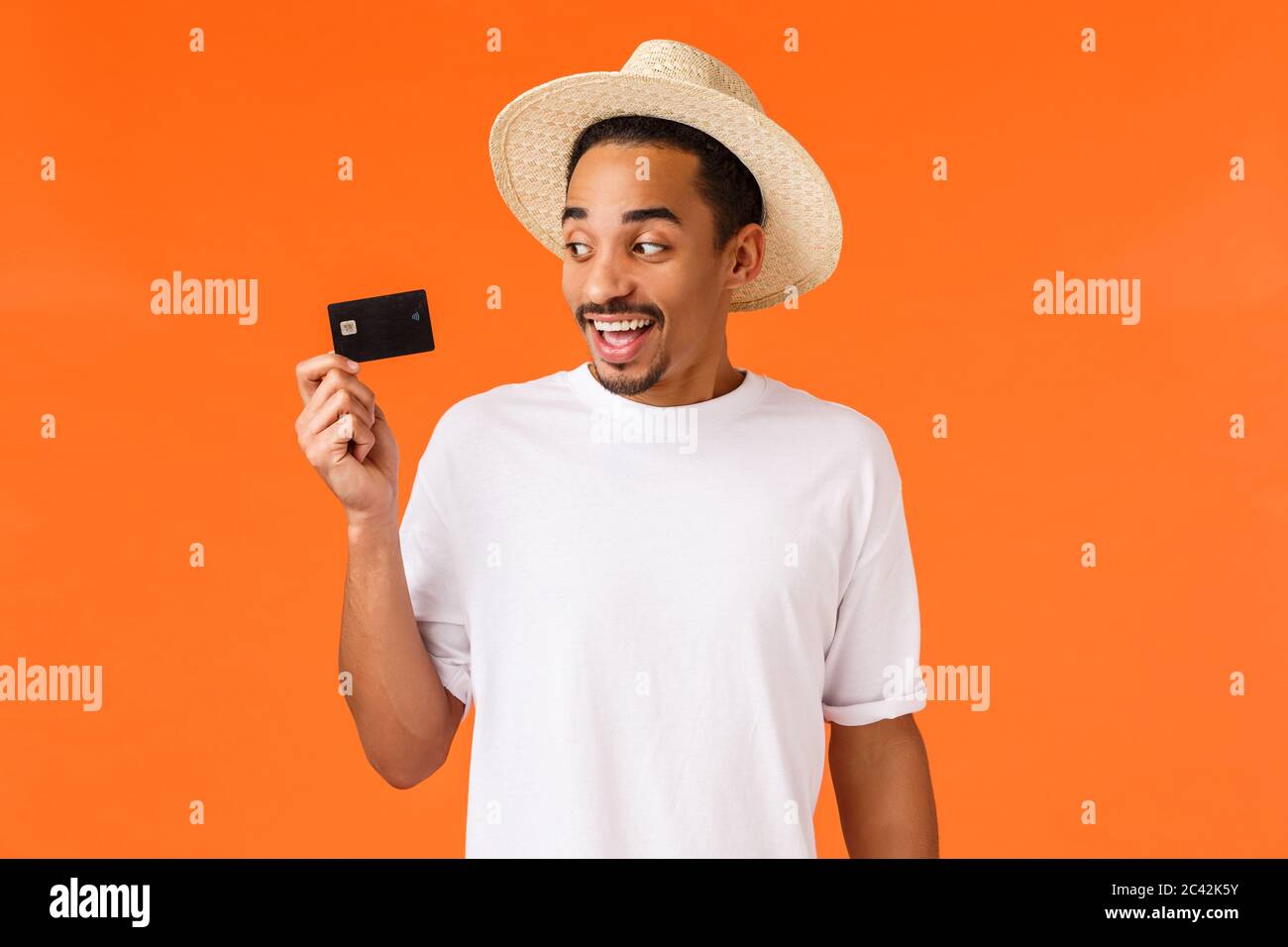 Cheerful, excité smiling african-american bel homme avec chapeau, tee-shirt blanc, à la carte de crédit et souriant heureux, à l'aide de dépôt, payer avec Banque D'Images