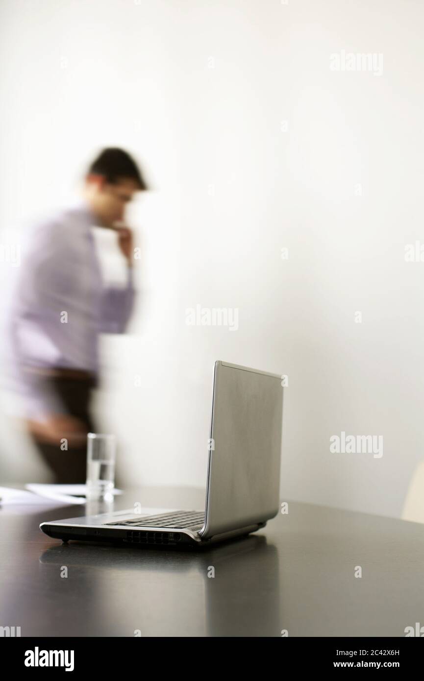 Homme d'affaires debout au téléphone derrière une table de conférence avec un ordinateur portable - bureau Banque D'Images