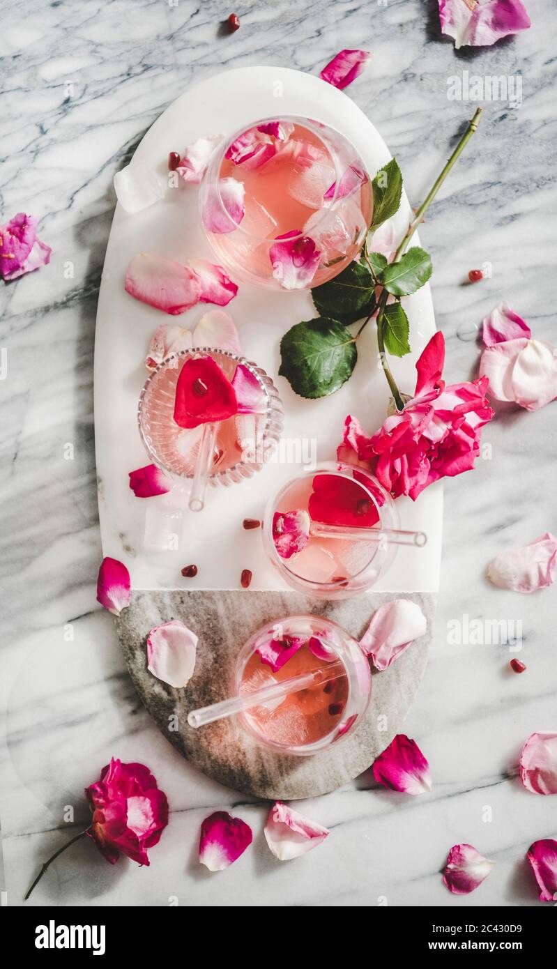 Boisson fraîche rafraîchissante en été. Pose plate de limonade rose avec glace en verre et pétales de rose sur une table de service ovale en marbre gris Banque D'Images