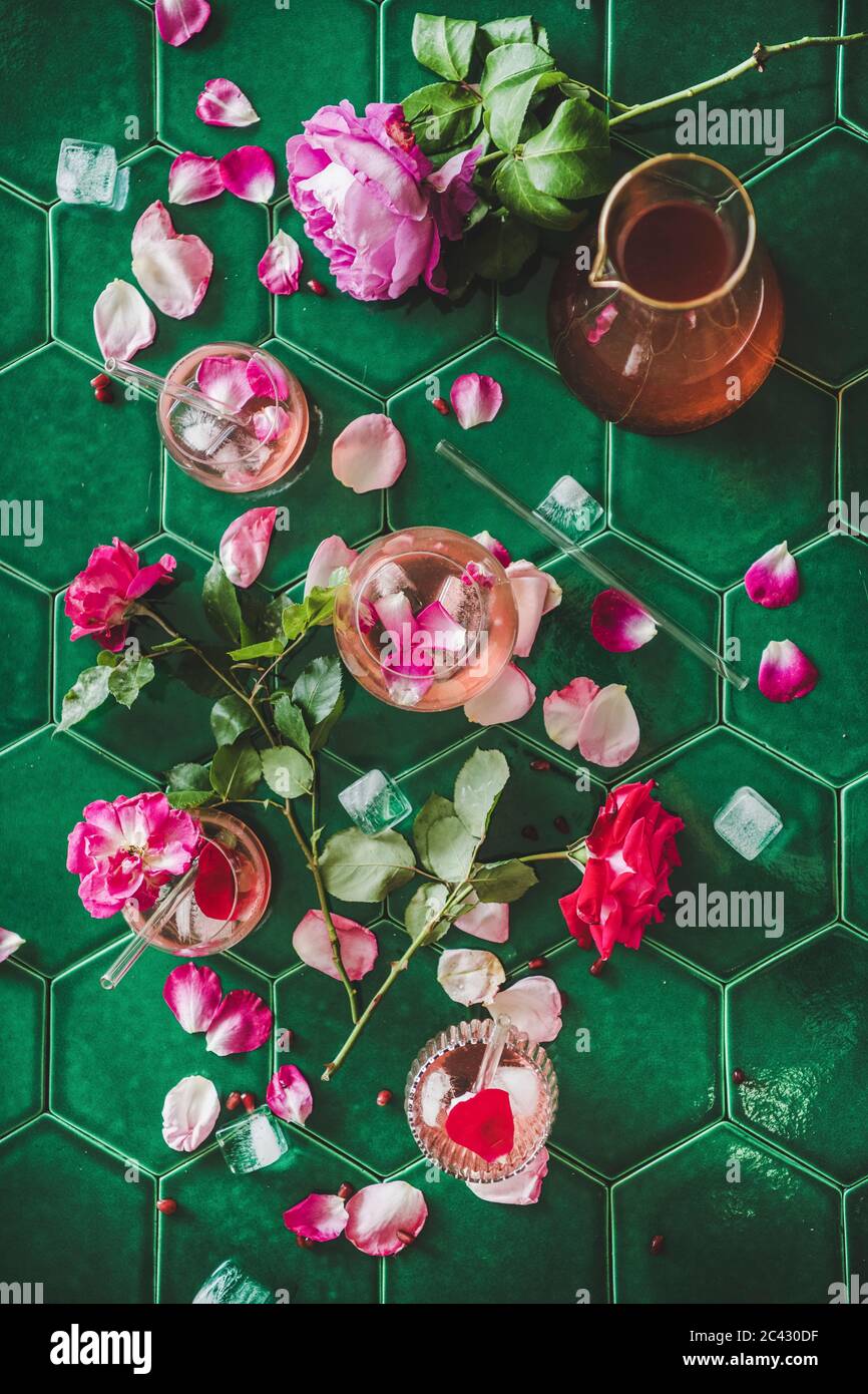 Boisson fraîche rafraîchissante en été. Pose plate de limonade rose avec glace en verre et verseuse et pétales de fleurs roses frais sur le dos de table en carreaux verts Banque D'Images