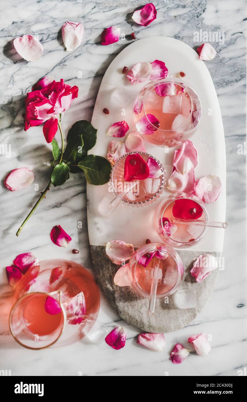 Boisson fraîche rafraîchissante en été. Pose plate de limonade rose avec glace en verre et verseuse et pétales de fleurs roses frais à bord sur une ta en marbre gris Banque D'Images