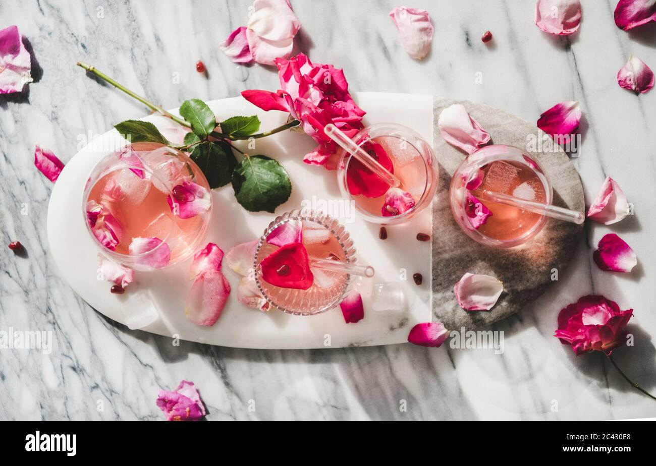 Boisson fraîche rafraîchissante en été. Pose plate de limonade rose avec glaçons en verre et pétales de fleurs roses frais sur plateau de service ovale au-dessus de gre Banque D'Images
