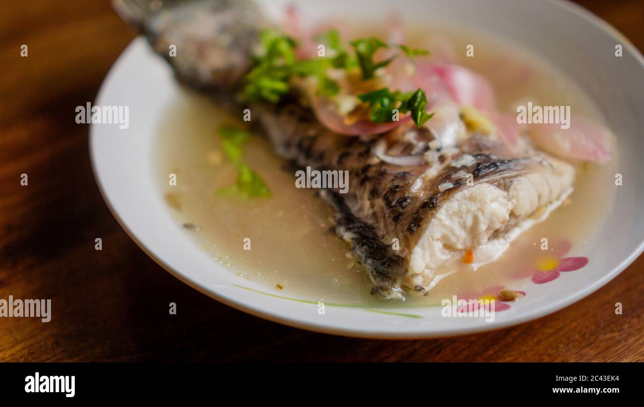 Poisson rôti cuit à la vapeur dans une sauce au citron avec oignon rouge et garni de coriandre. Banque D'Images