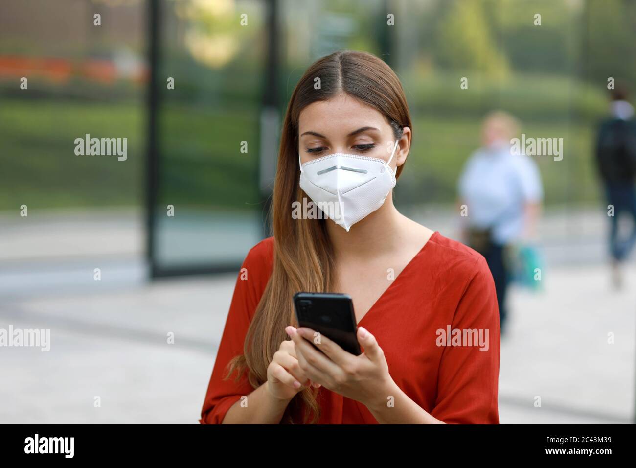 Jeune femme portant le masque KN95 FFP2 en utilisant l'application de téléphone mobile dans City Street pour faciliter le suivi de contact et l'auto diagnostic en réponse à la maladie de coronavirus Banque D'Images