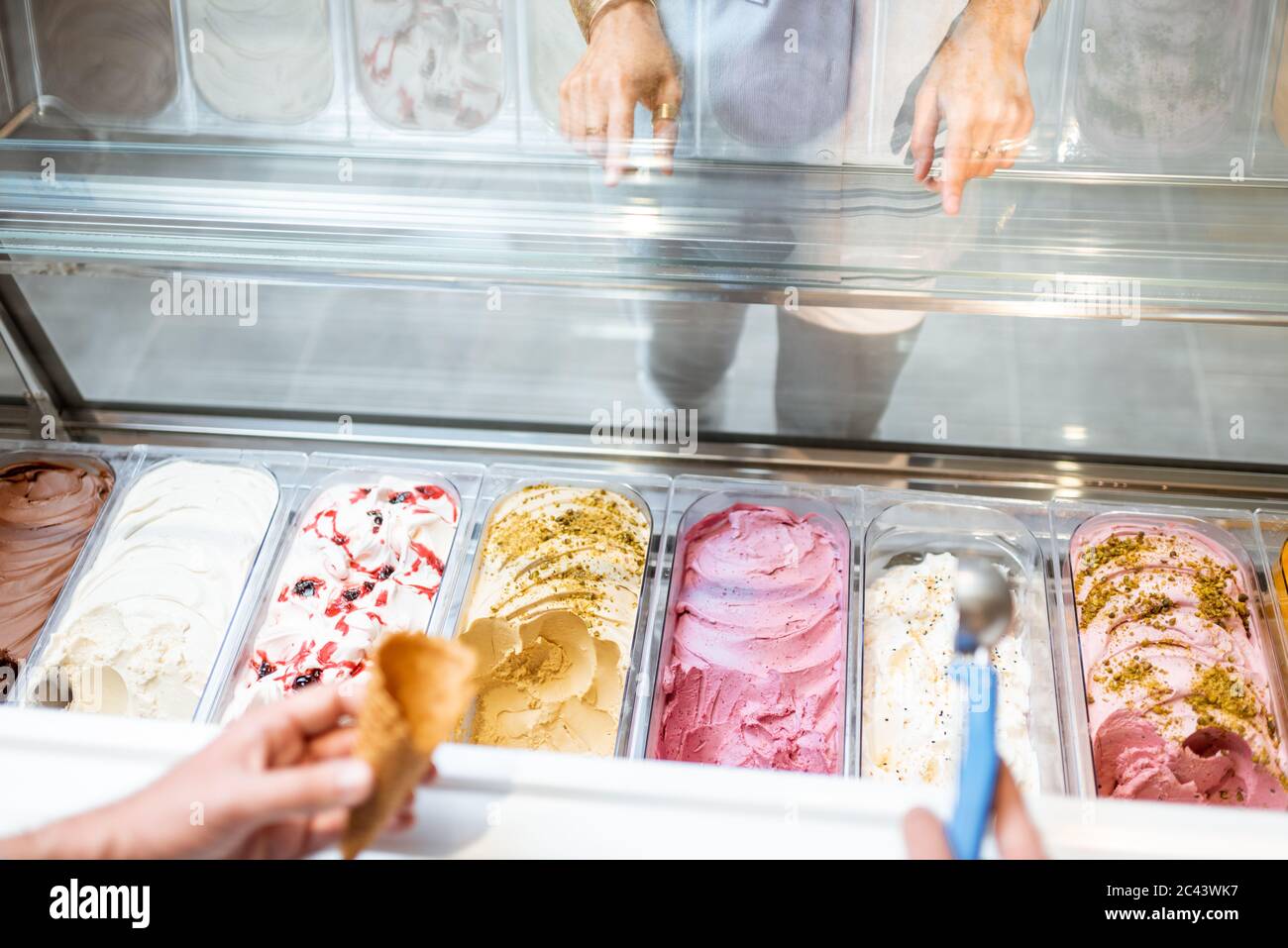 Le vendeur cueillia de la crème glacée avec une cuillère du réfrigérateur dans le magasin. Vue d'en haut sur un plateau rempli de crème glacée aux saveurs différentes Banque D'Images