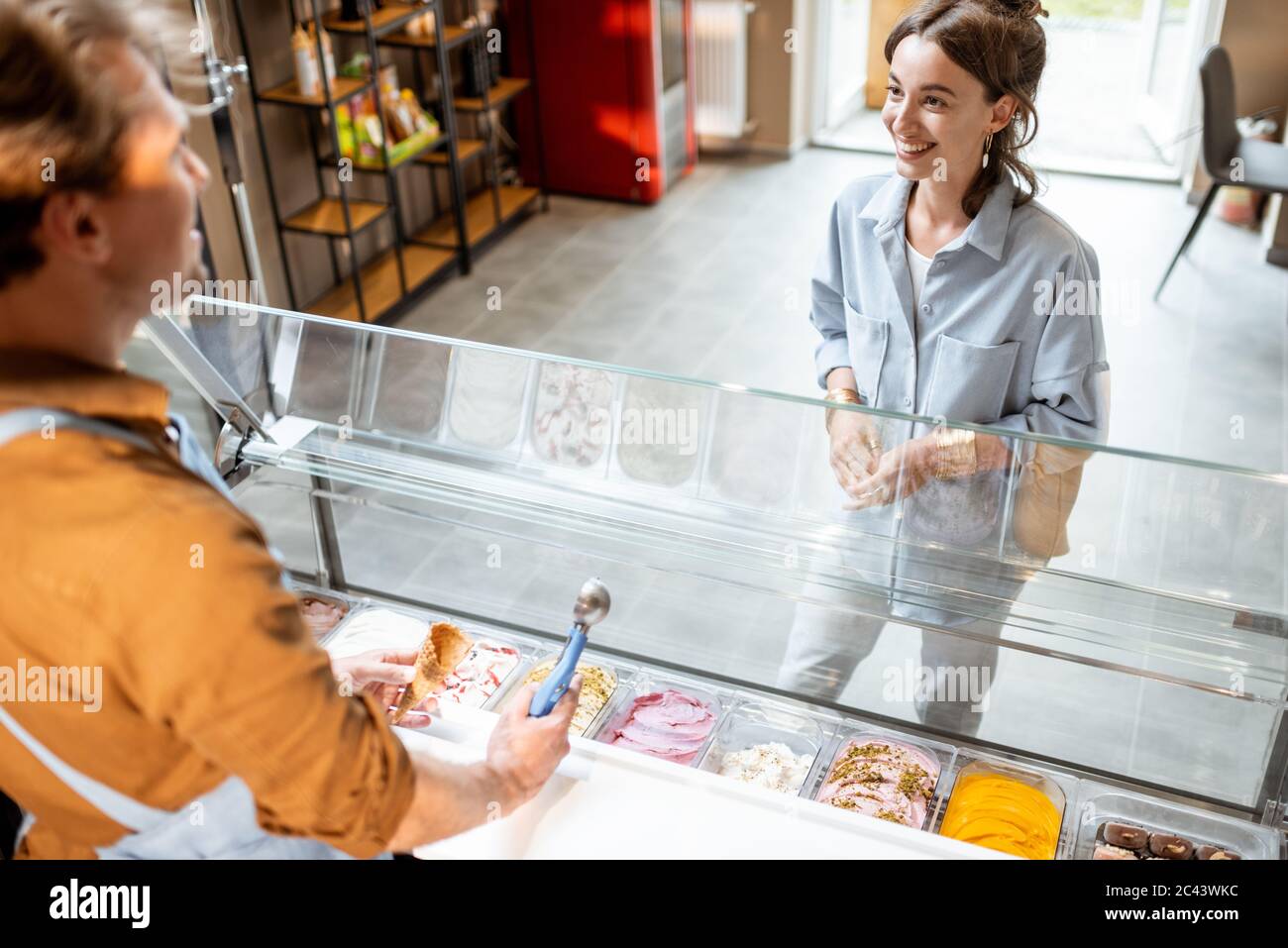 Jeune cliente de choix de crème glacée, debout avec un vendeur près de la fenêtre du magasin Banque D'Images