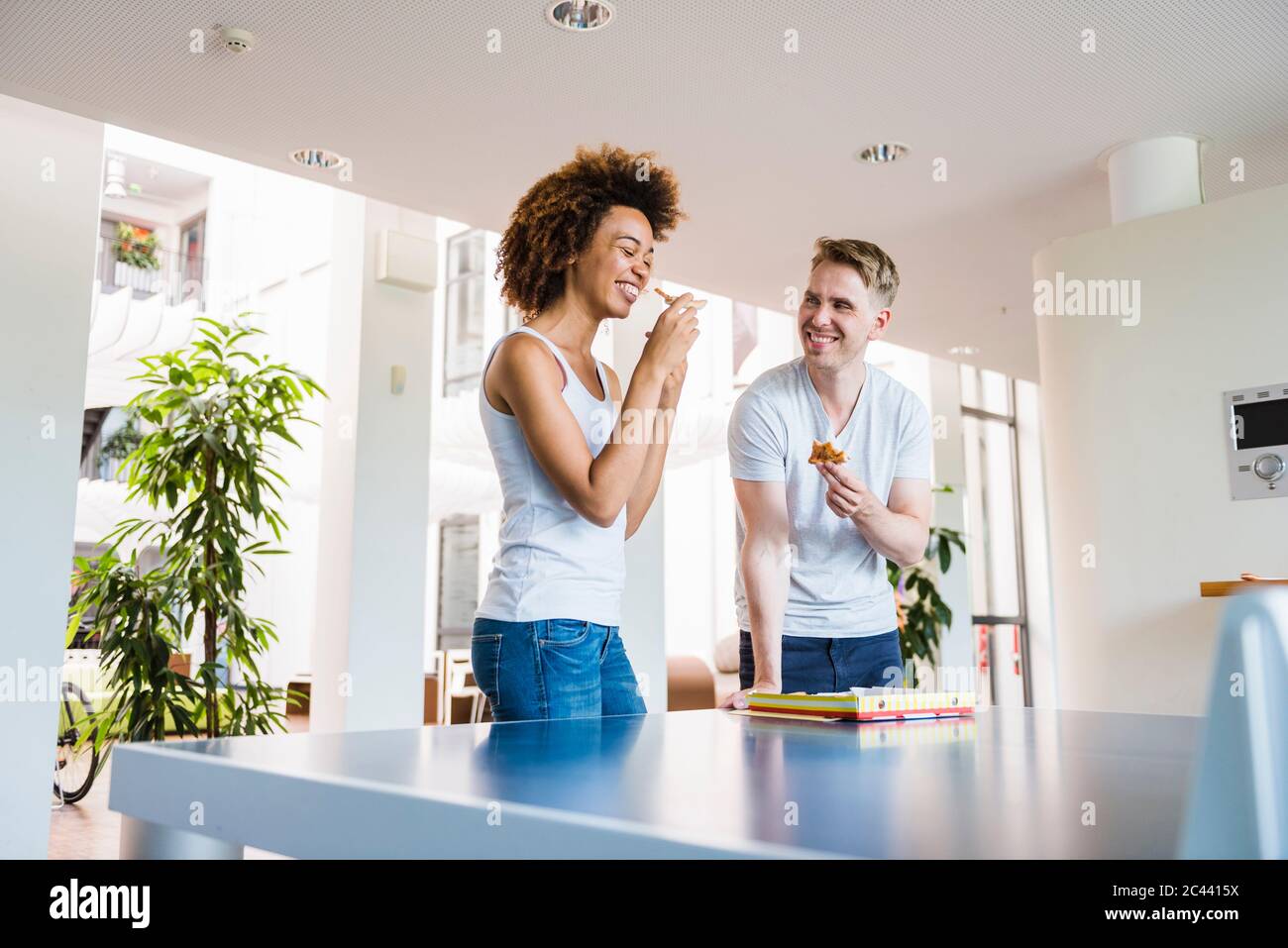 Les jeunes gens d'affaires partagent une pizza pour le déjeuner dans un bureau moderne avec table de ping-pong Banque D'Images